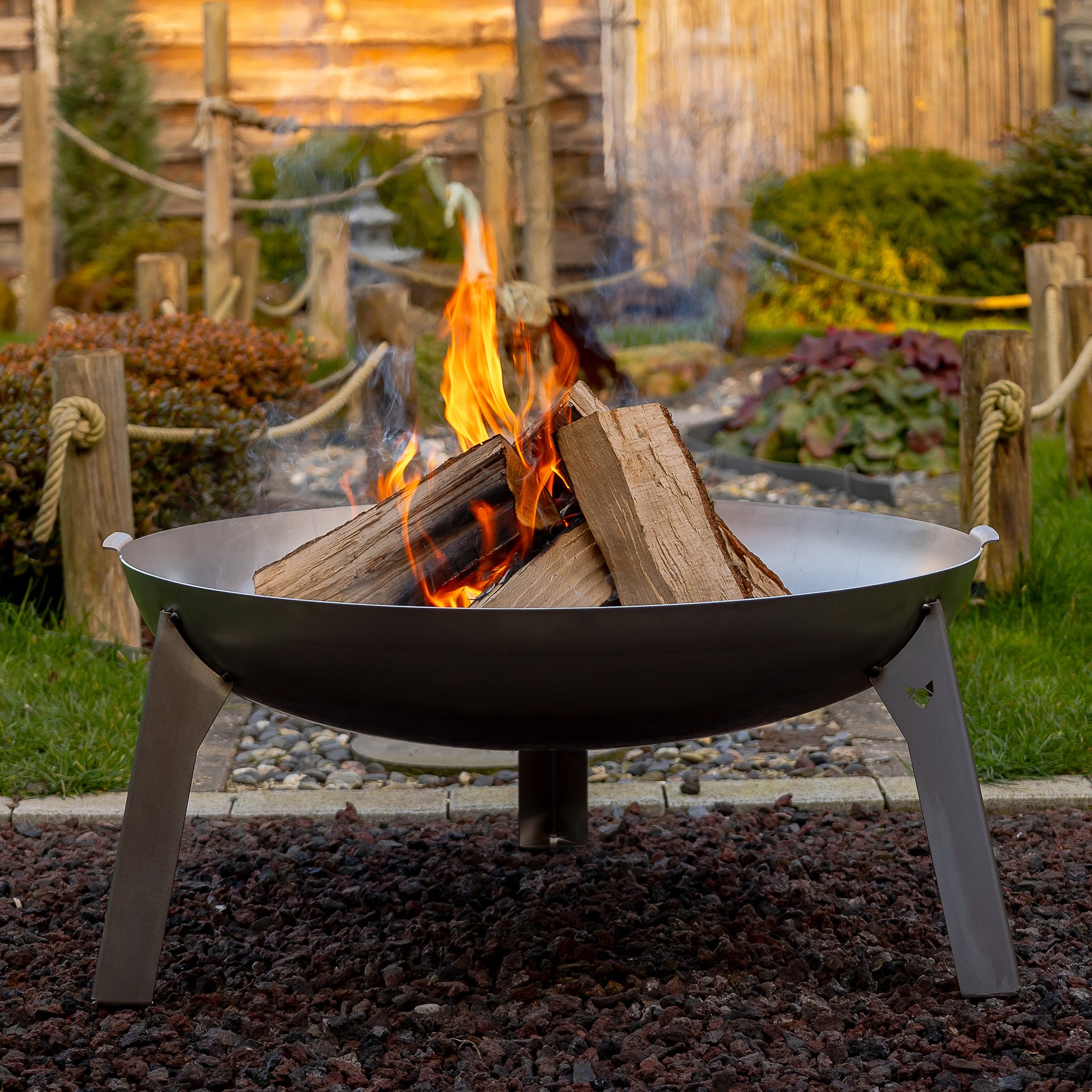 Ein schönes Lagerfeuer in der Feuerschale Edelstahl, welche auf einem Kiesbett steht in einem schön angelegten Garten..