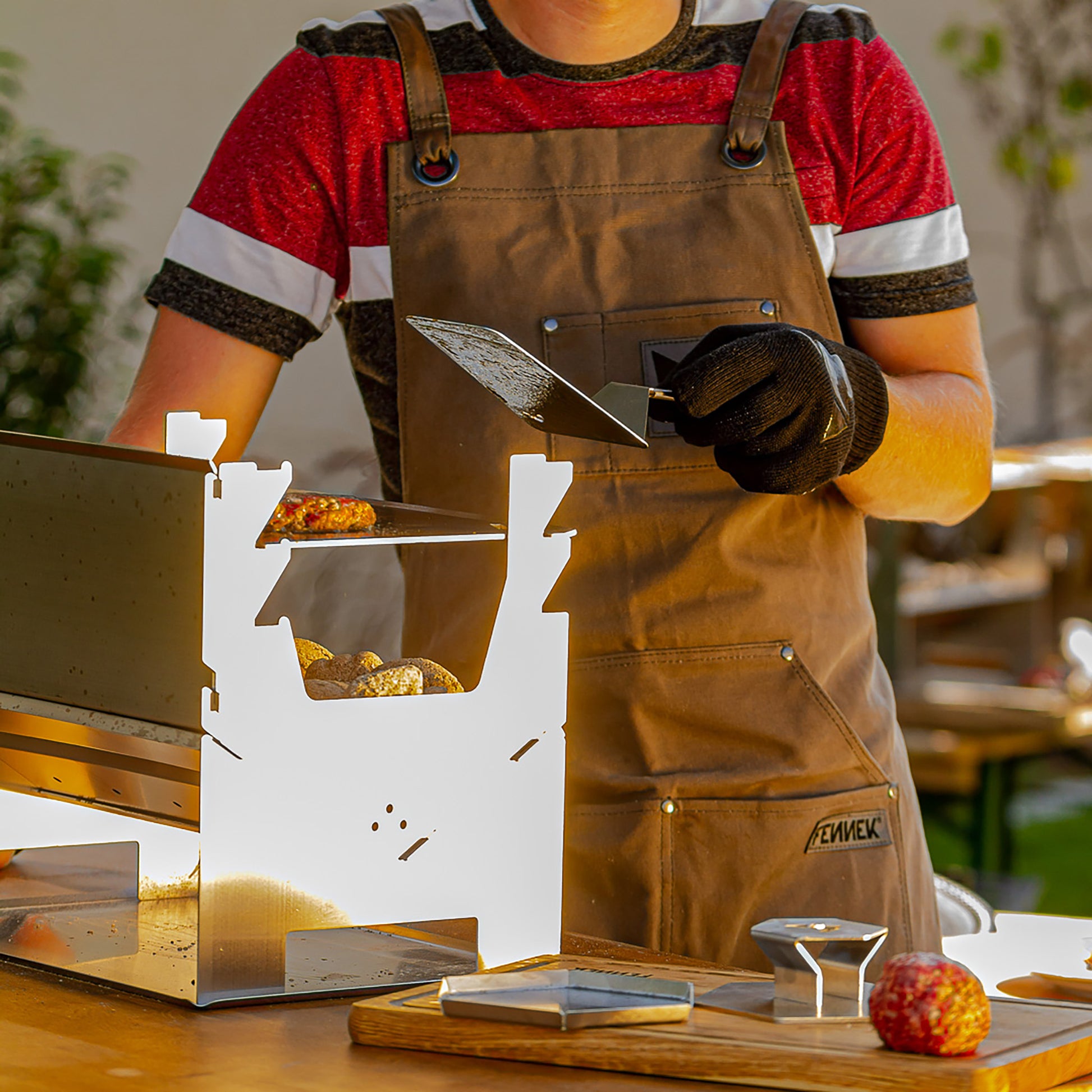 BBQ-Wender im Einsatz wird gehalten von einer Person mit Grillschürze und Grillhandschuh.