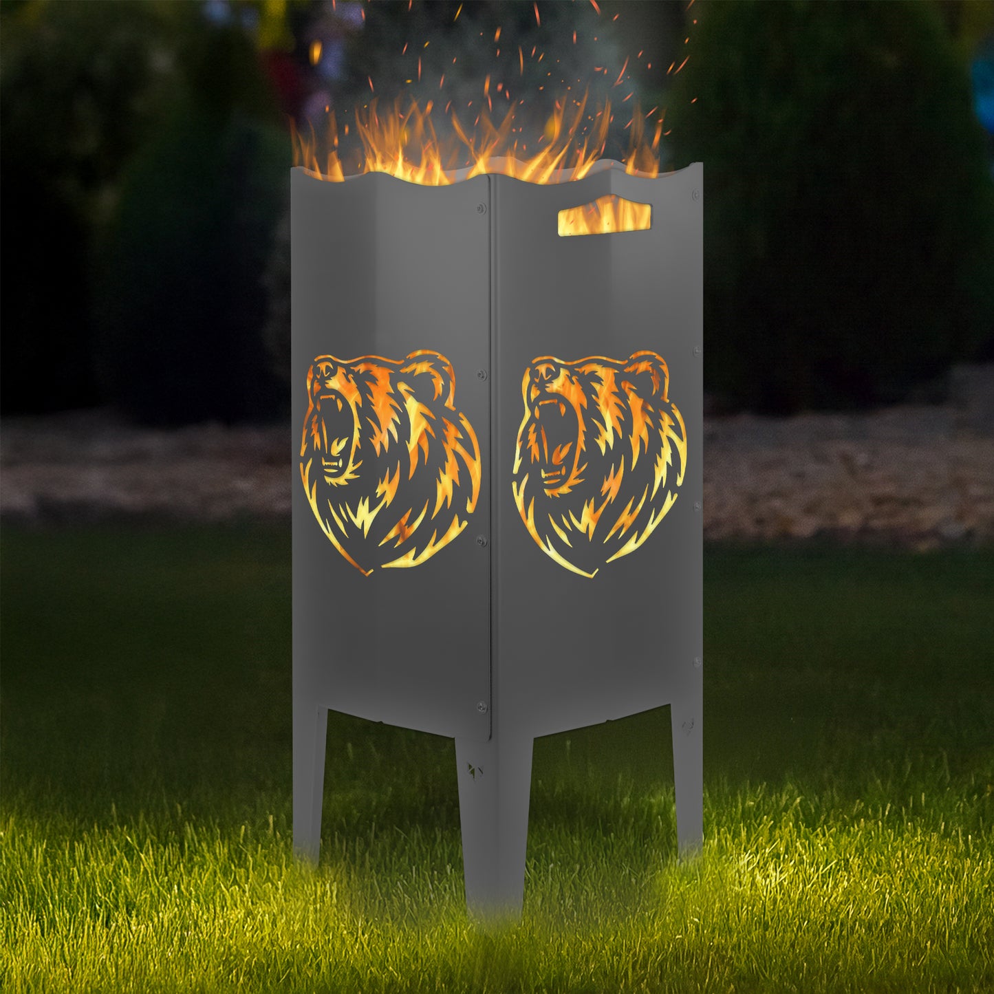 FENNEK Feuersäule Stahl mit dem Motiv Bär - in der Feuersäule brennt ein Feuer, man sieht das Motiv sehr schön leuchten in der Abenddämmerung in einem Garten. Die Feuersäule steht auf Gras.