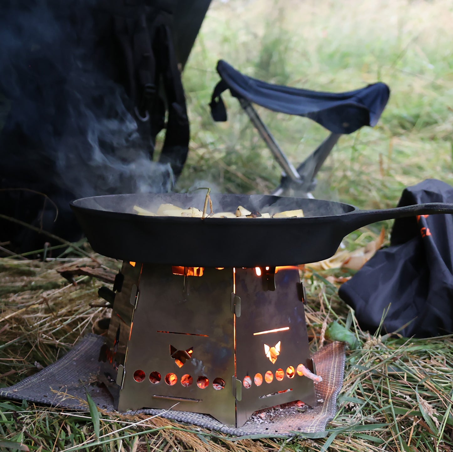 Der Hobokocher FENNEK Basic mit Erweiterungsset in Aktion beim Braten mit einer schwarzen Gußpfanne auf einer Wiese.