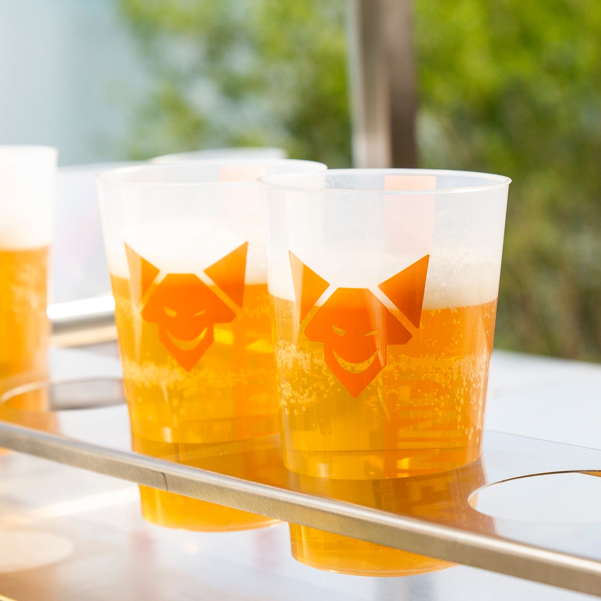 Mehrere mit Bier gefüllte Mehrwegbecher, im Fokus 2 Becher in einer Halterung aus Edelstahl