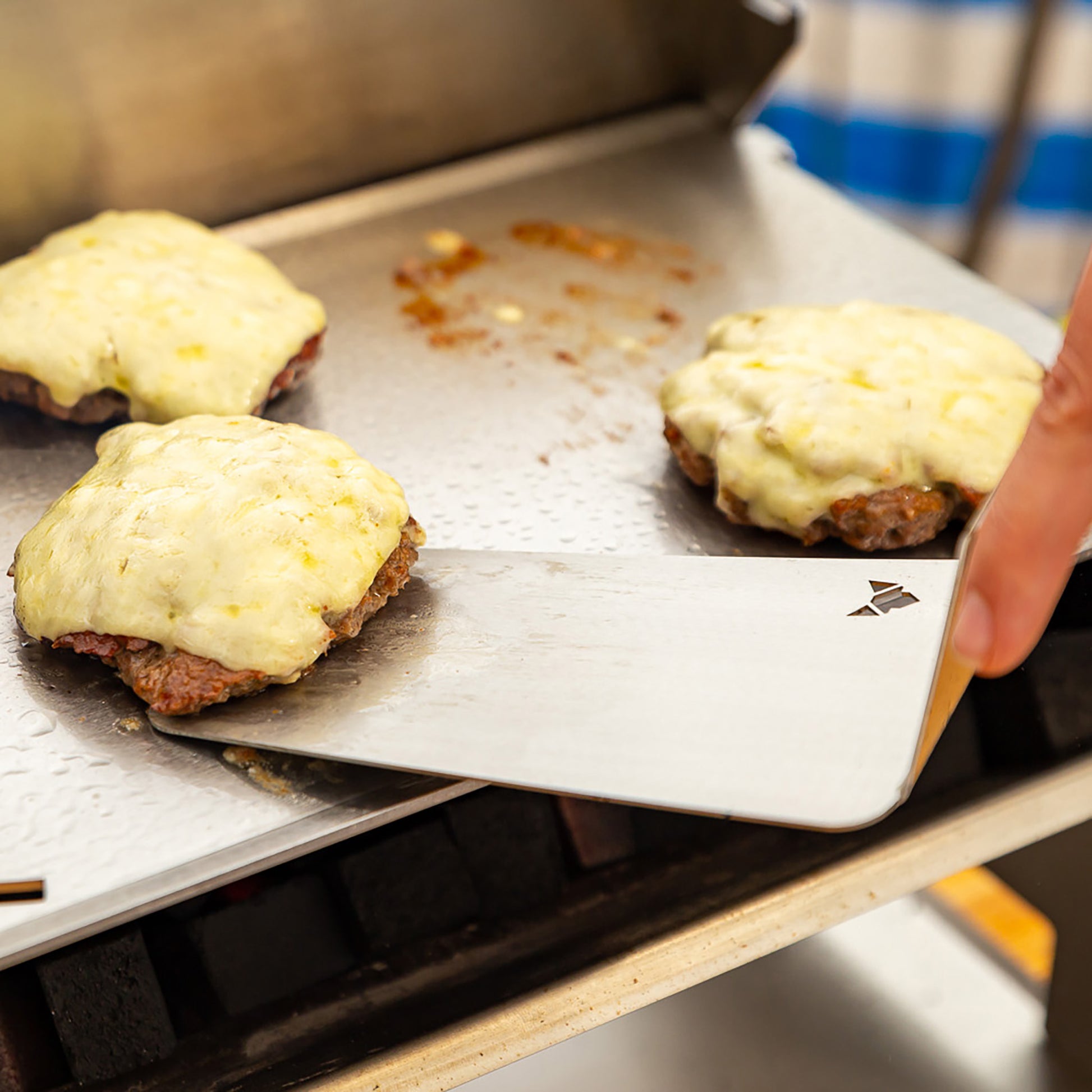 Edelstahl BBQ-Wender hebt mit Käse überbackene Burgerpatties von der Grillplatte