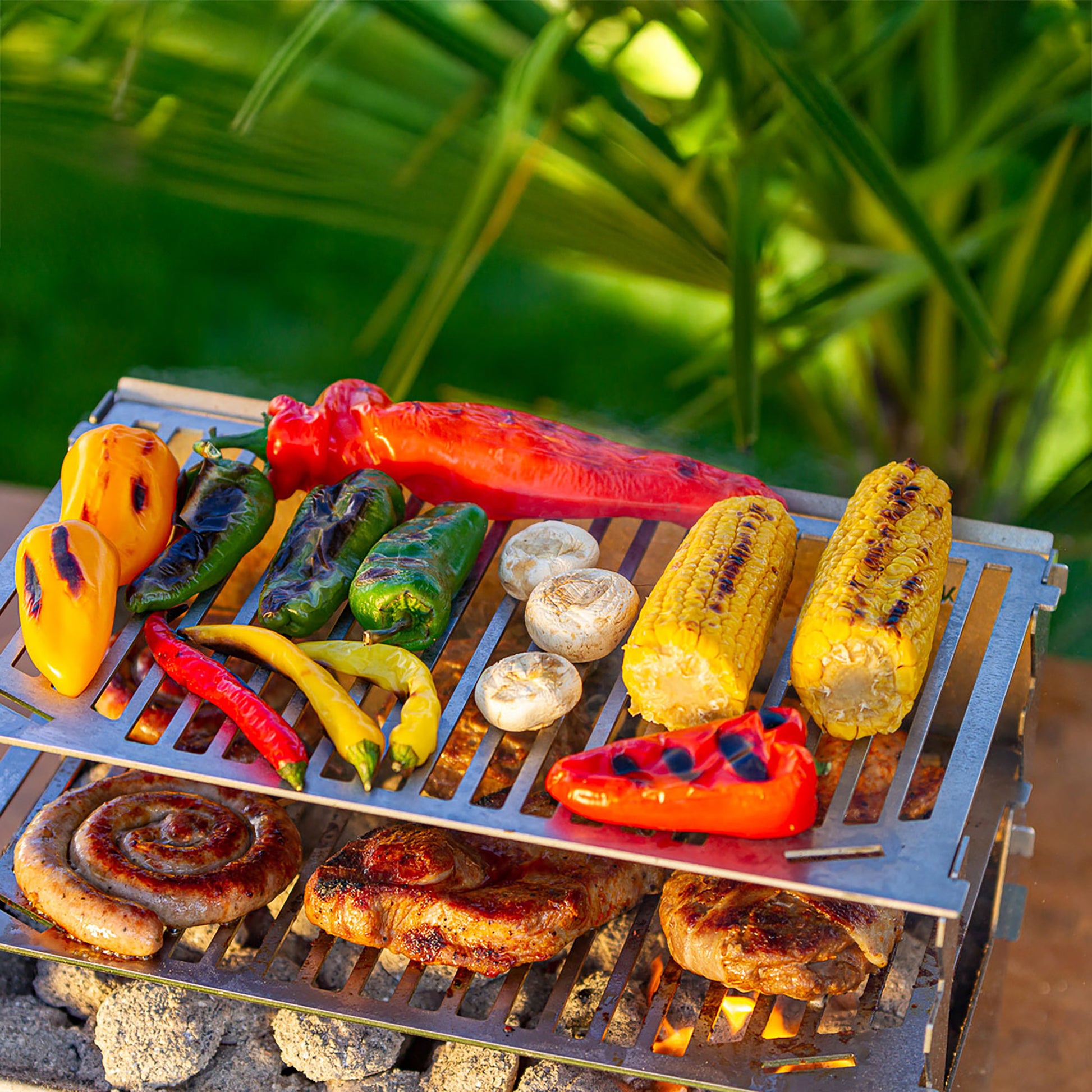 Blick von oben auf den Holzkohlegrill mit 2 Grillroste auf 2 Höhen mit Fleisch unten und buntem Gemüse oben.