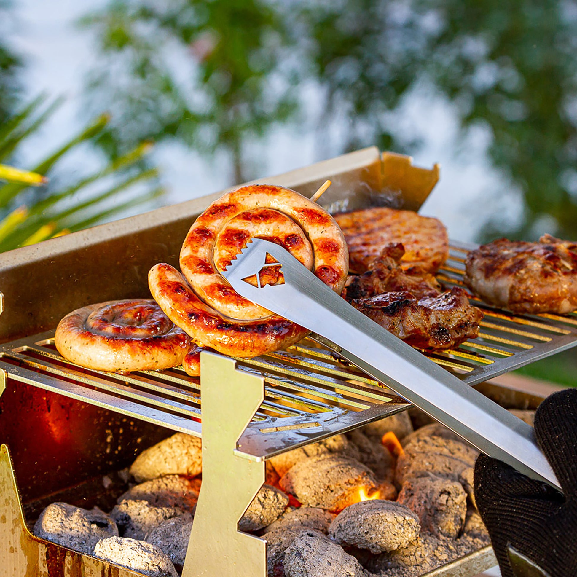 Grillzange hebt eine gebratene Bratwurstschnecke vom Grillrost.