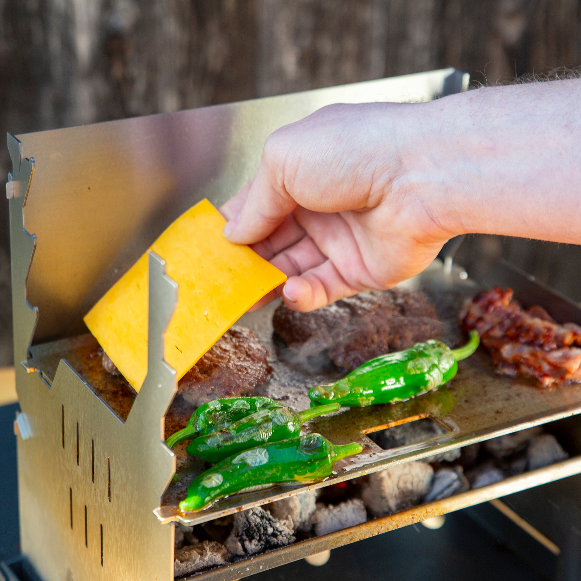 Zubereiten von Burger auf einer Plancha für den FENNEK Grill. Eine Hand legt Käse auf das Patty