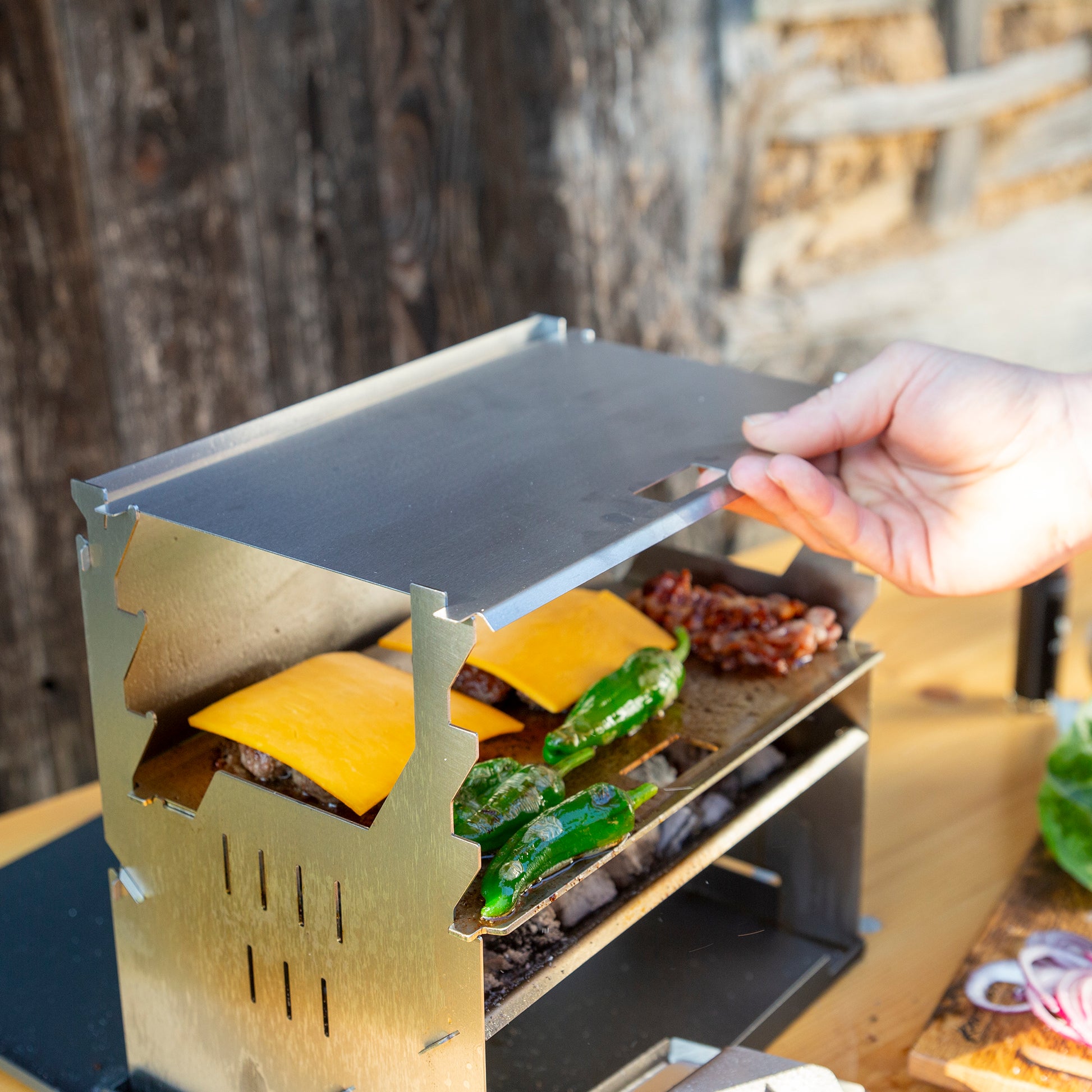 Eine Hand verstellt den Deckel eines Holzkohlegrills auf dem Cheeseburger zubereitet werden.