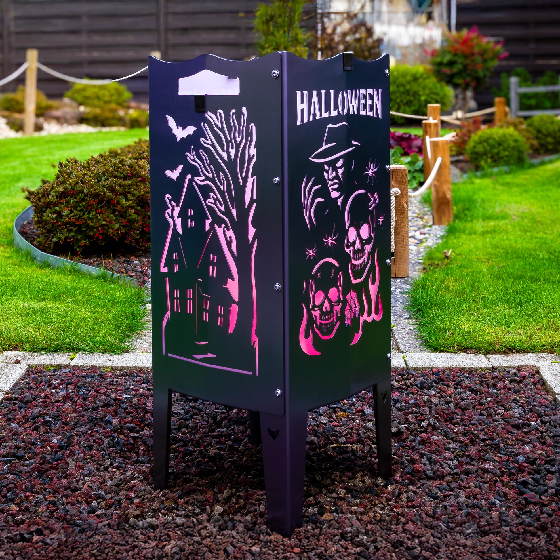 Die FENNEK Halloween Feuersäule lt. Edition steht in einem schönen Garten  und wird mit LED-Strahler von Innen beleuchtet. Der Feuerkorb kann aber auch mit normalem Feuer betrieben werden. Made in Germany.