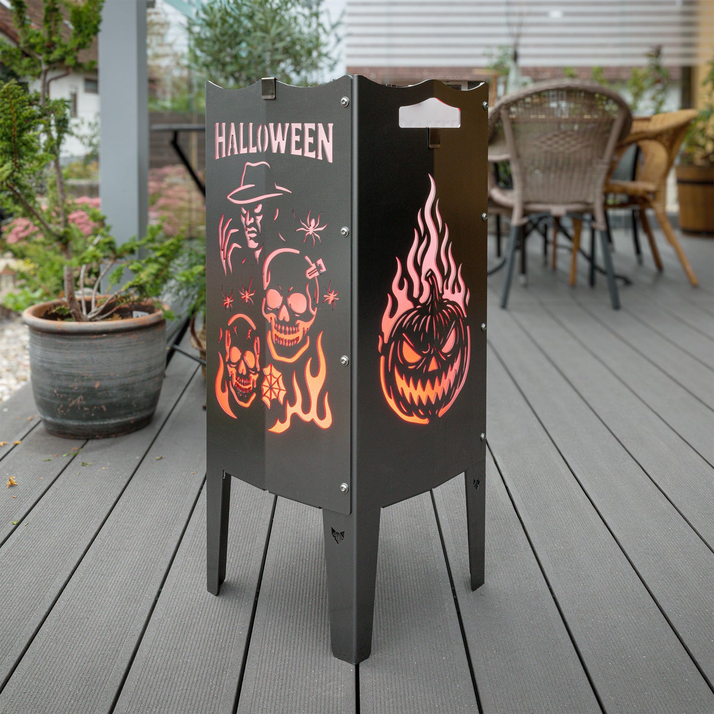 Die FENNEK Halloween Feuersäule lt. Edition steht in einem schönen Garten auf einer Terrasse und wird mit LED-Strahler von Innen beleuchtet. Der Feuerkorb kann aber auch mit normalem Feuer betrieben werden. Made in Germany.
