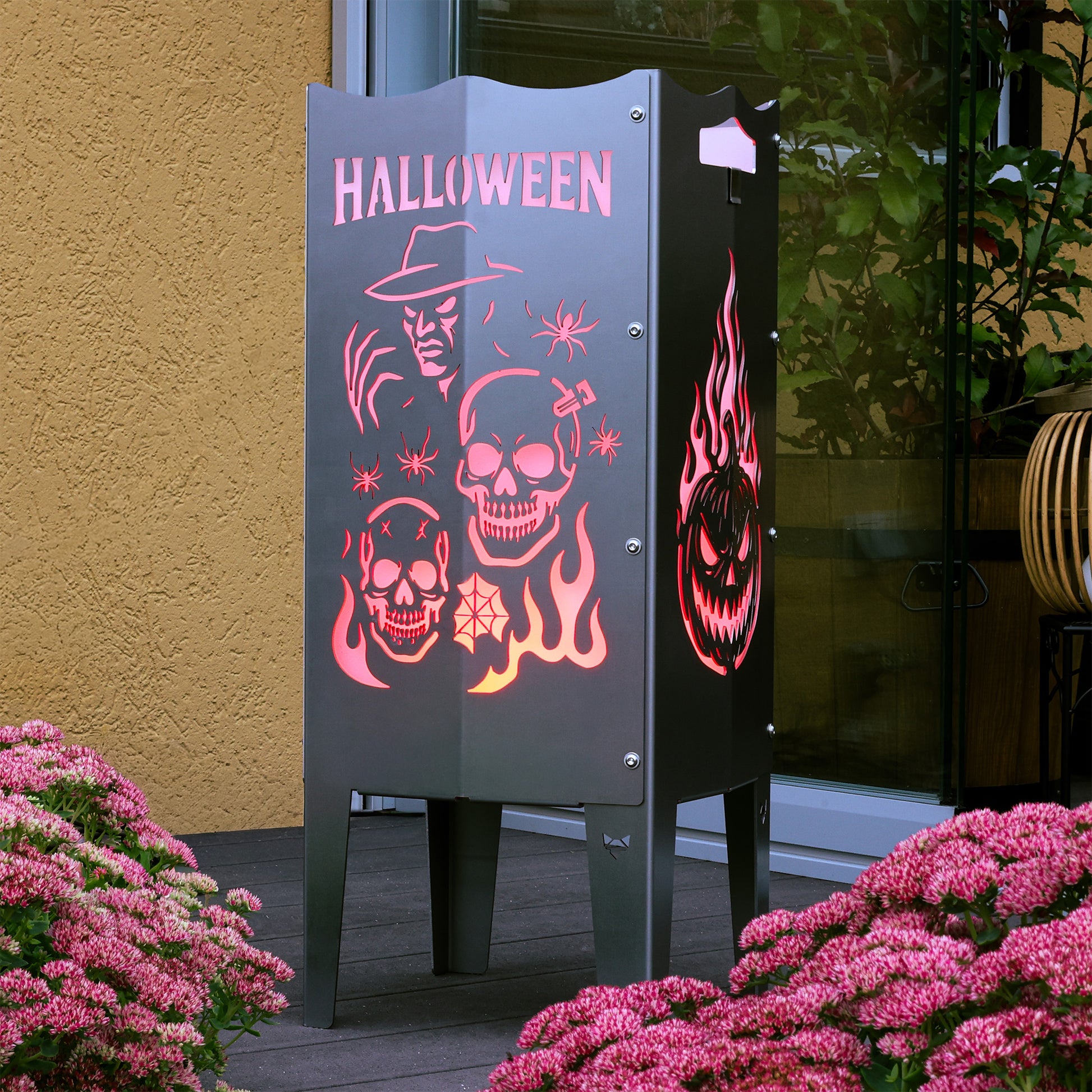 Die FENNEK Halloween Feuersäule lt. Edition steht in einem schönen Garten auf einer Terrasse und wird mit LED-Strahler von Innen beleuchtet. Der Feuerkorb kann aber auch mit normalem Feuer betrieben werden. Made in Germany.