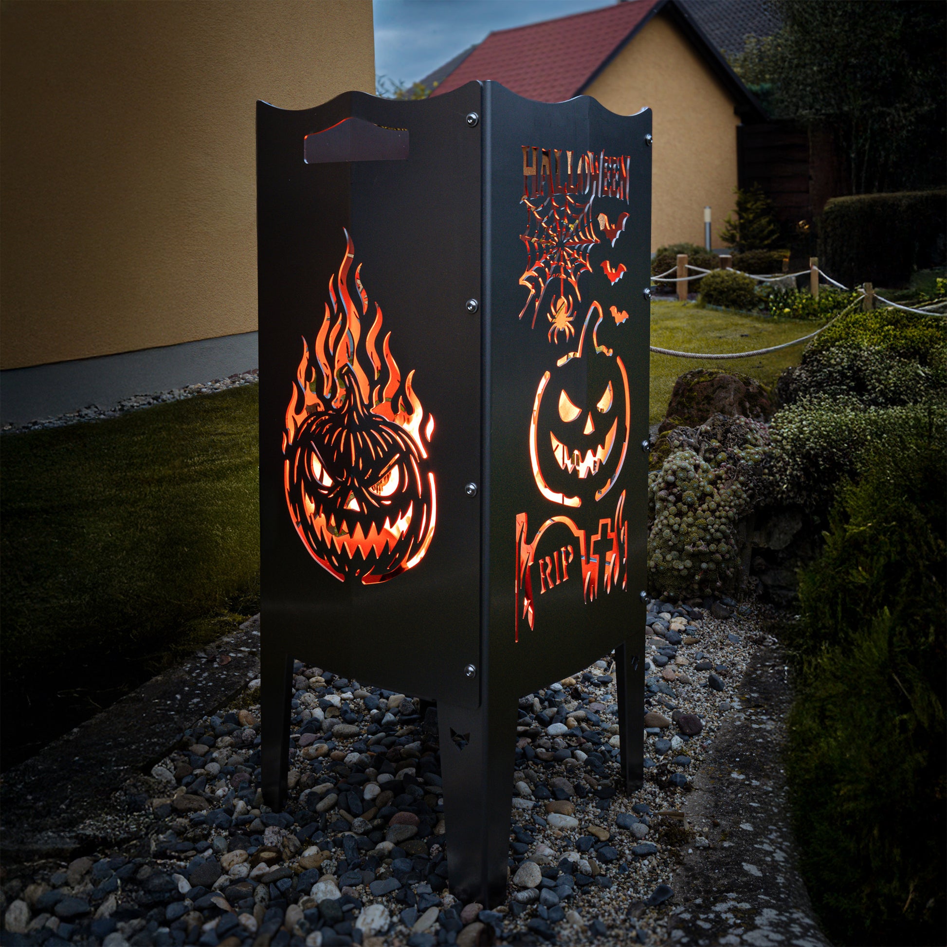 Die FENNEK Halloween Feuersäule lt. Edition steht in einem schönen Garten und wird Feuerholz von Innen beleuchtet. Der Feuerkorb kann aber auch mit einem LED-Strahler von Innen betrieben werden. Made in Germany.