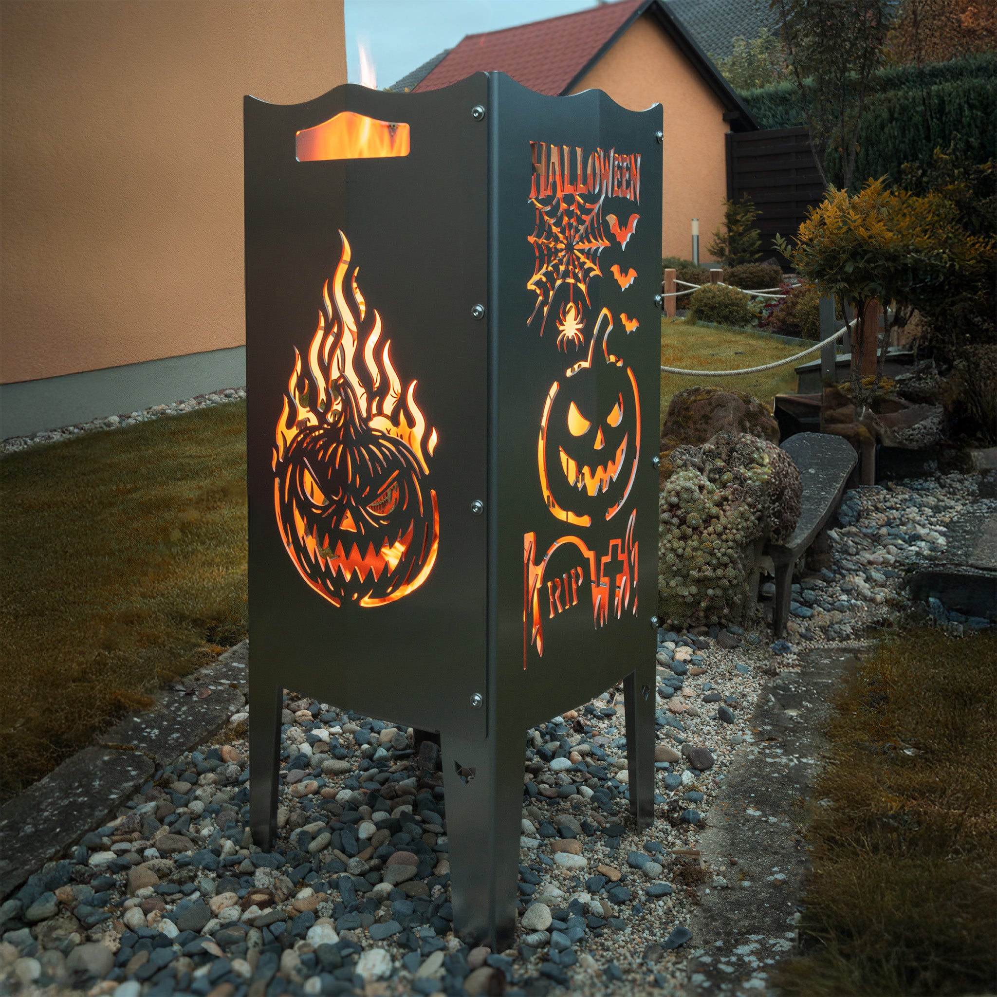 Die FENNEK Halloween Feuersäule lt. Edition steht in einem schönen Garten und wird Feuerholz von Innen beleuchtet. Der Feuerkorb kann aber auch mit einem LED-Strahler von Innen betrieben werden. Made in Germany.