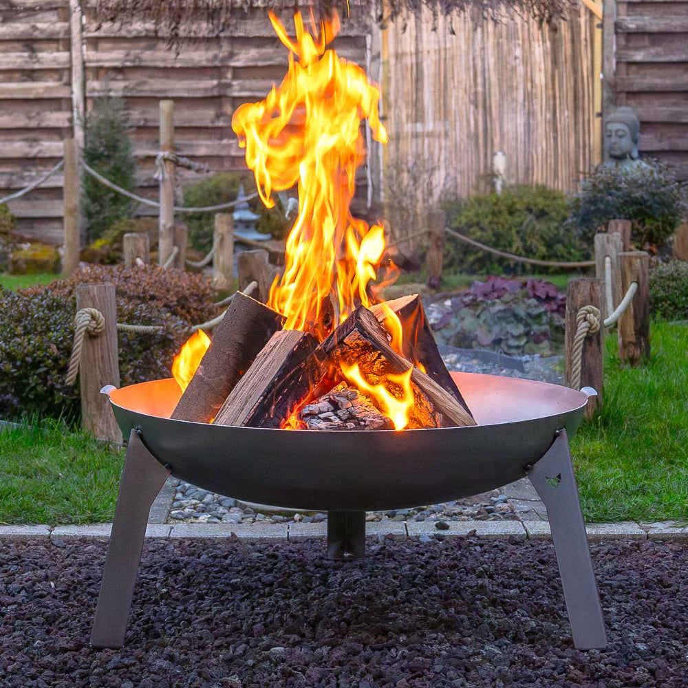 Ein schönes Lagerfeuer in der Feuerschale Edelstahl, welche auf einem Kiesbett steht in einem schön angelegten Garten..