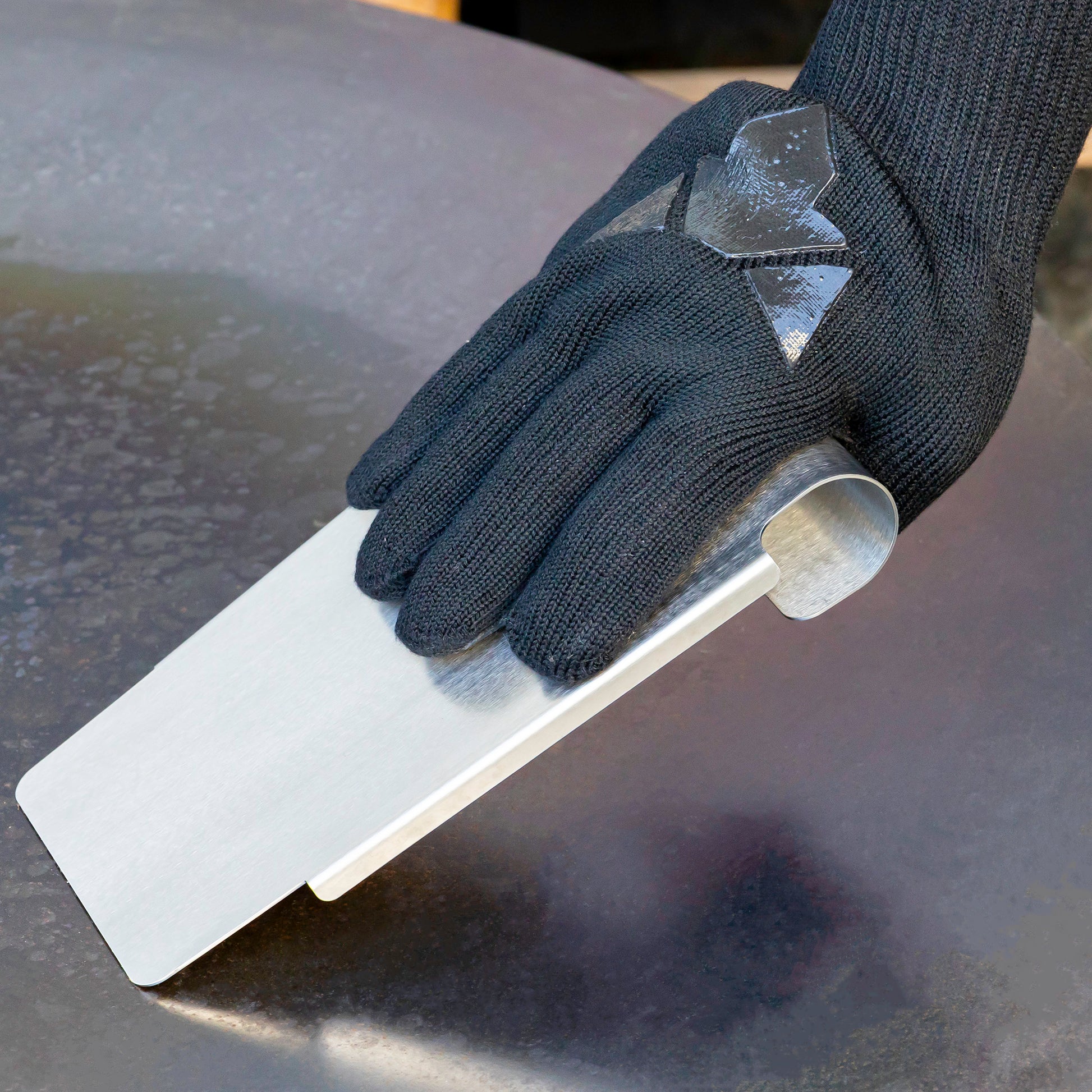 Grillspachtel wird von Handschuh gehalten und schabt auf Feuerplatte
