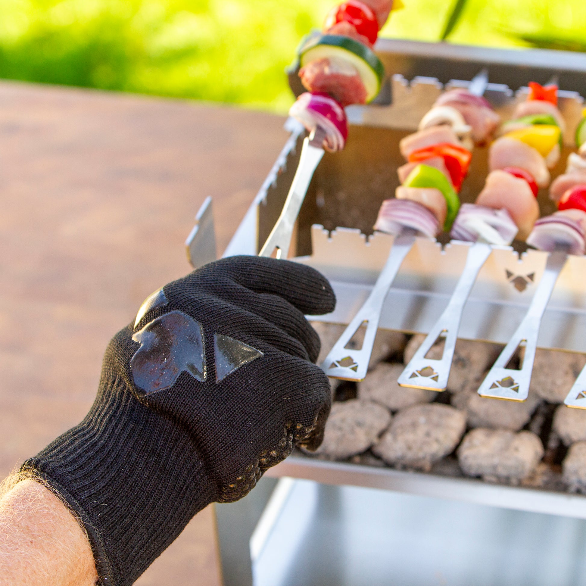 Grillhandschuh der gerade einen Grillspieß über dem Grill dreht