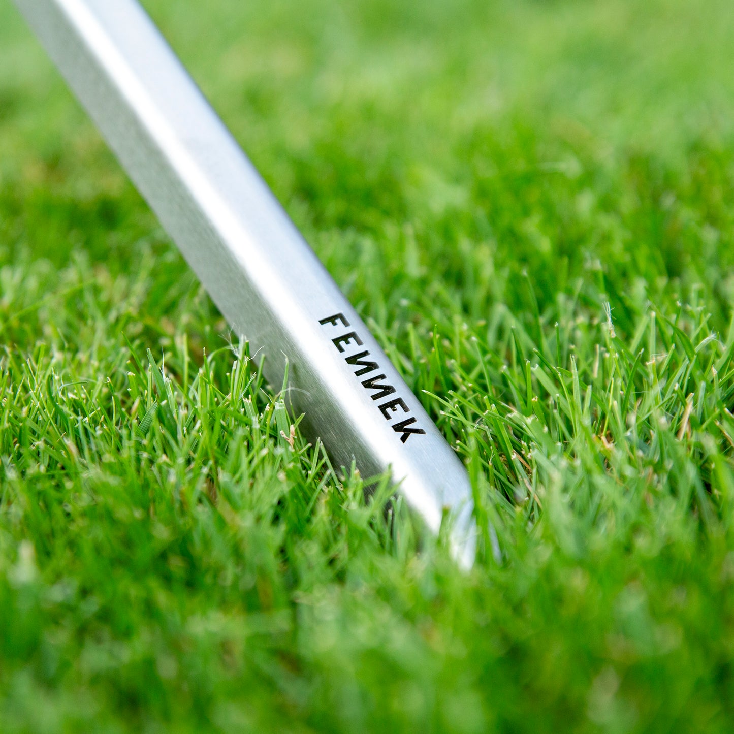 Nahaufnahme FENNEK-Schriftzug am Endes eines Standbein das im saftig grünen Rasen steht.