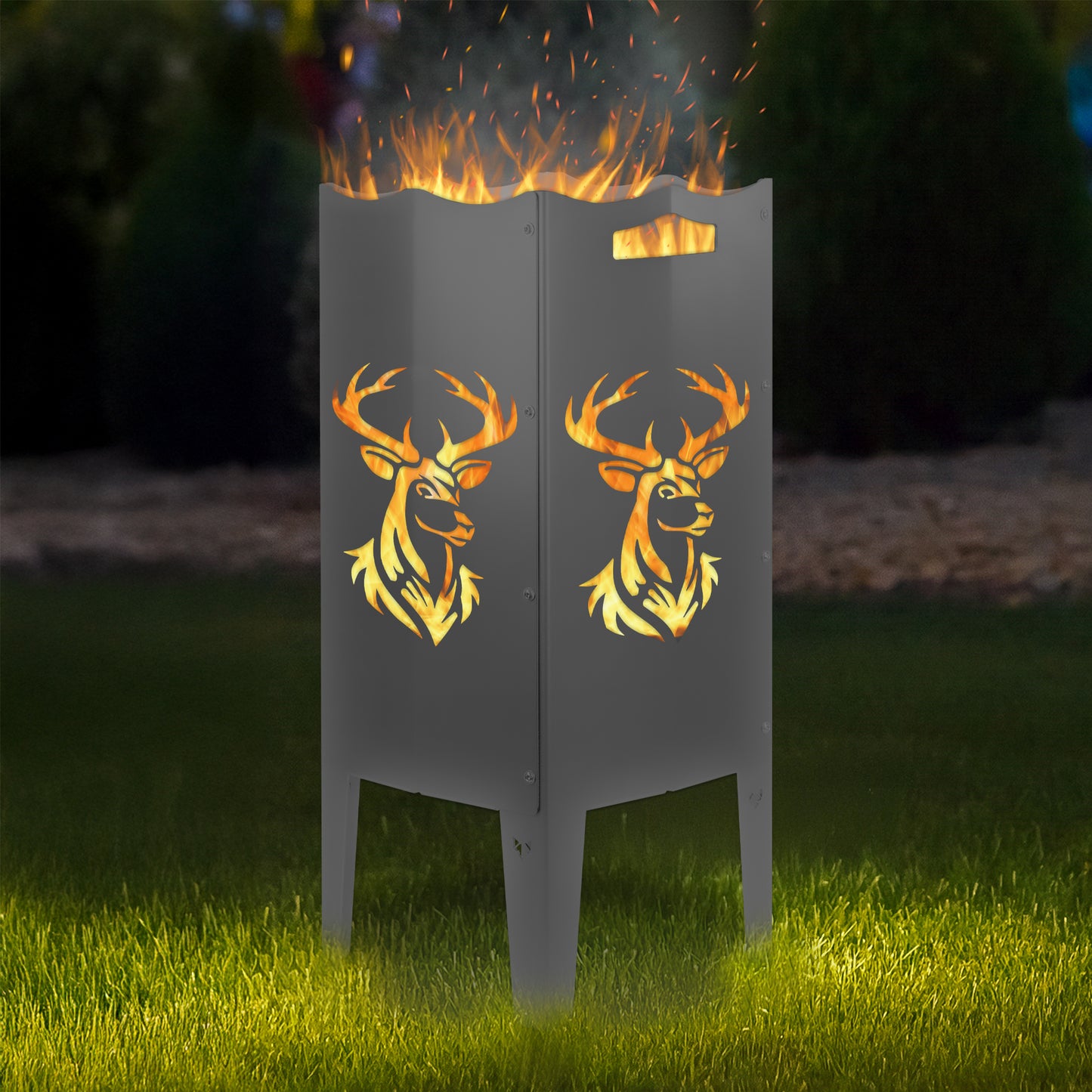 FENNEK Feuersäule Stahl mit dem Motiv Hirsch - in der Feuersäule brennt ein Feuer, man sieht das Motiv sehr schön leuchten in der Abenddämmerung in einem Garten. Die Feuersäule steht auf Gras.