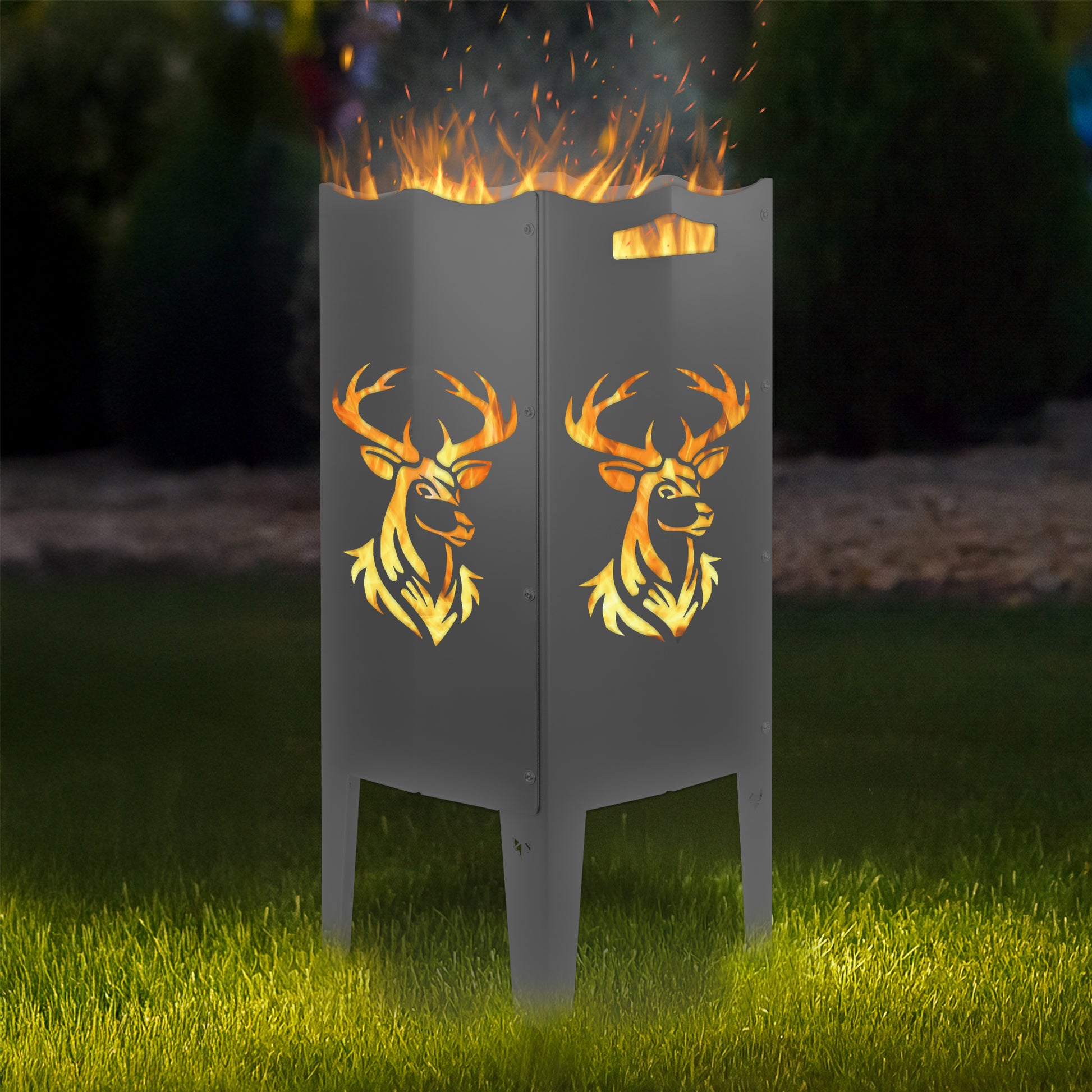 FENNEK Feuersäule Stahl mit dem Motiv Hirsch - in der Feuersäule brennt ein Feuer, man sieht das Motiv sehr schön leuchten in der Abenddämmerung in einem Garten. Die Feuersäule steht auf Gras.