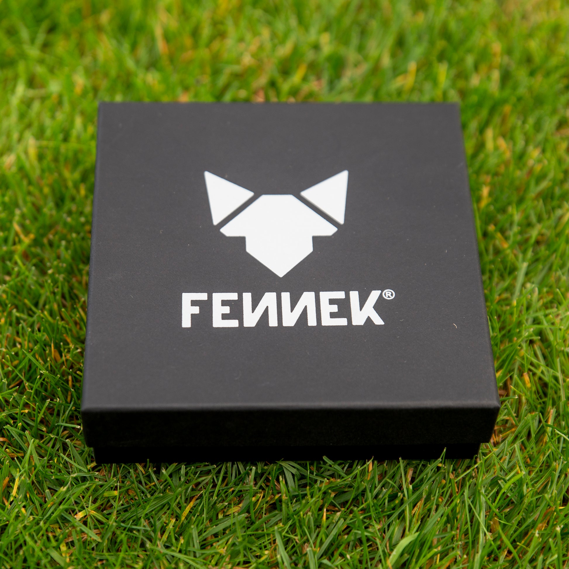 Edle schwarze Geschenkverpackung mit hellgrauem FENNEK Logo-Aufdruck auf der Oberseite, liegt auf grünem Rasen