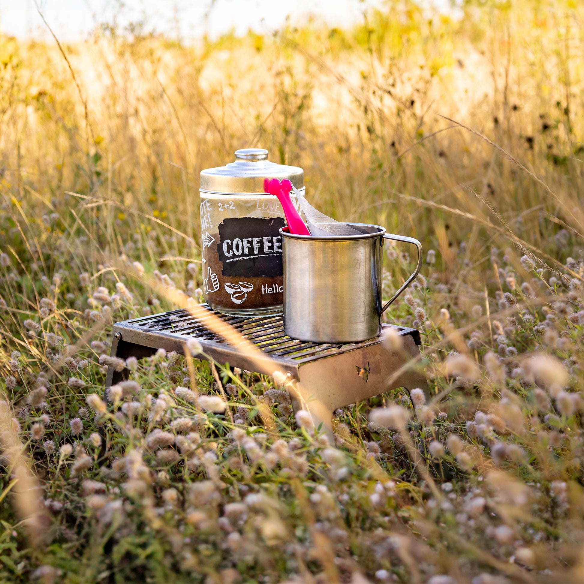 Klapprost als Tisch auf einer wilden Sommerwiese genutzt für einen Behälter mit Kaffeepulver darin und eine Edelstahl-Tasse