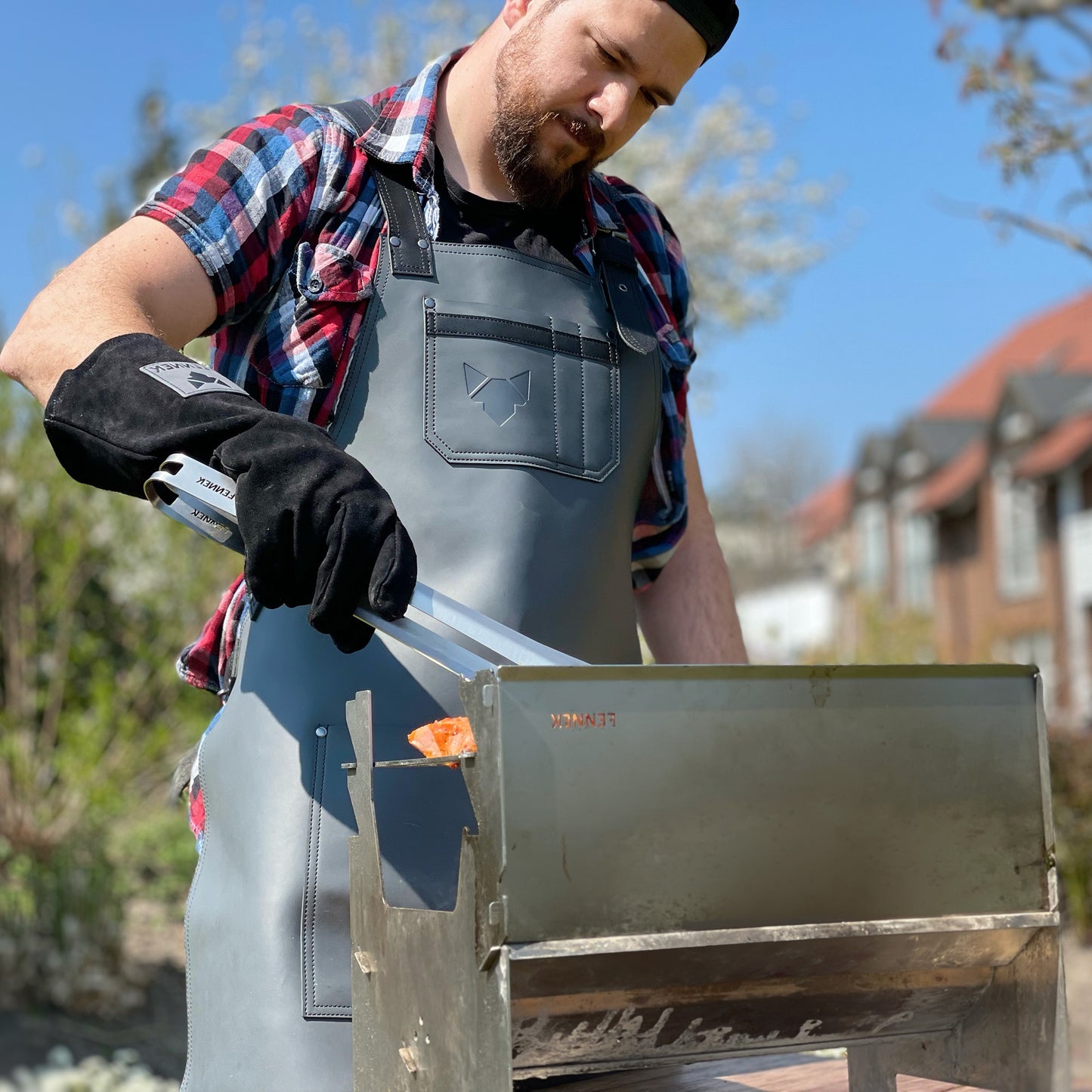 Mann mit Leder-Grillschürze beim Grillen, mit Grillzange in der Hand