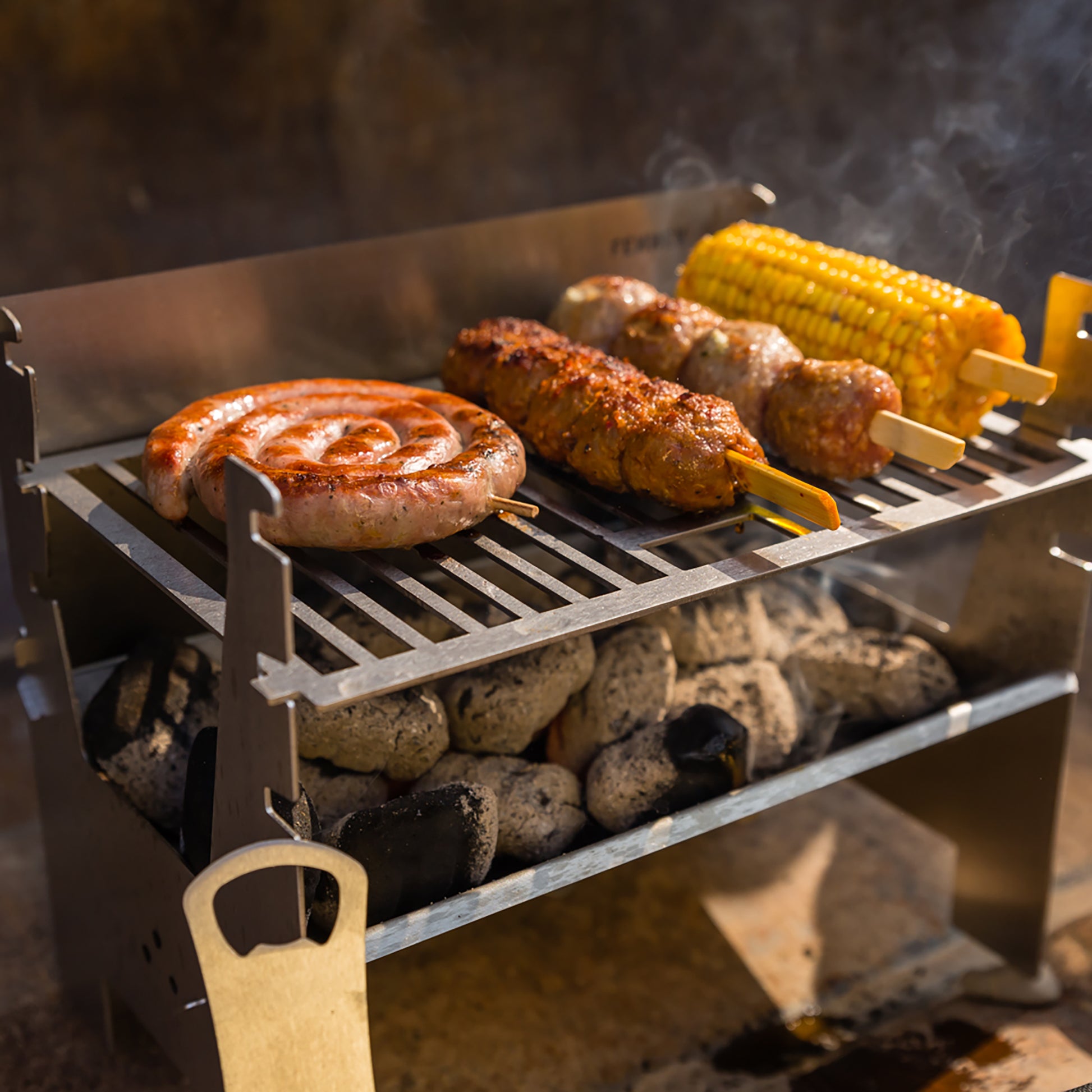 Lecker gebratene Bratwurstschnecke und weiteres Fleisch am Spieß und ein Maiskolben auf einem mobilen Holzkohlegrill aus Edelstahl.