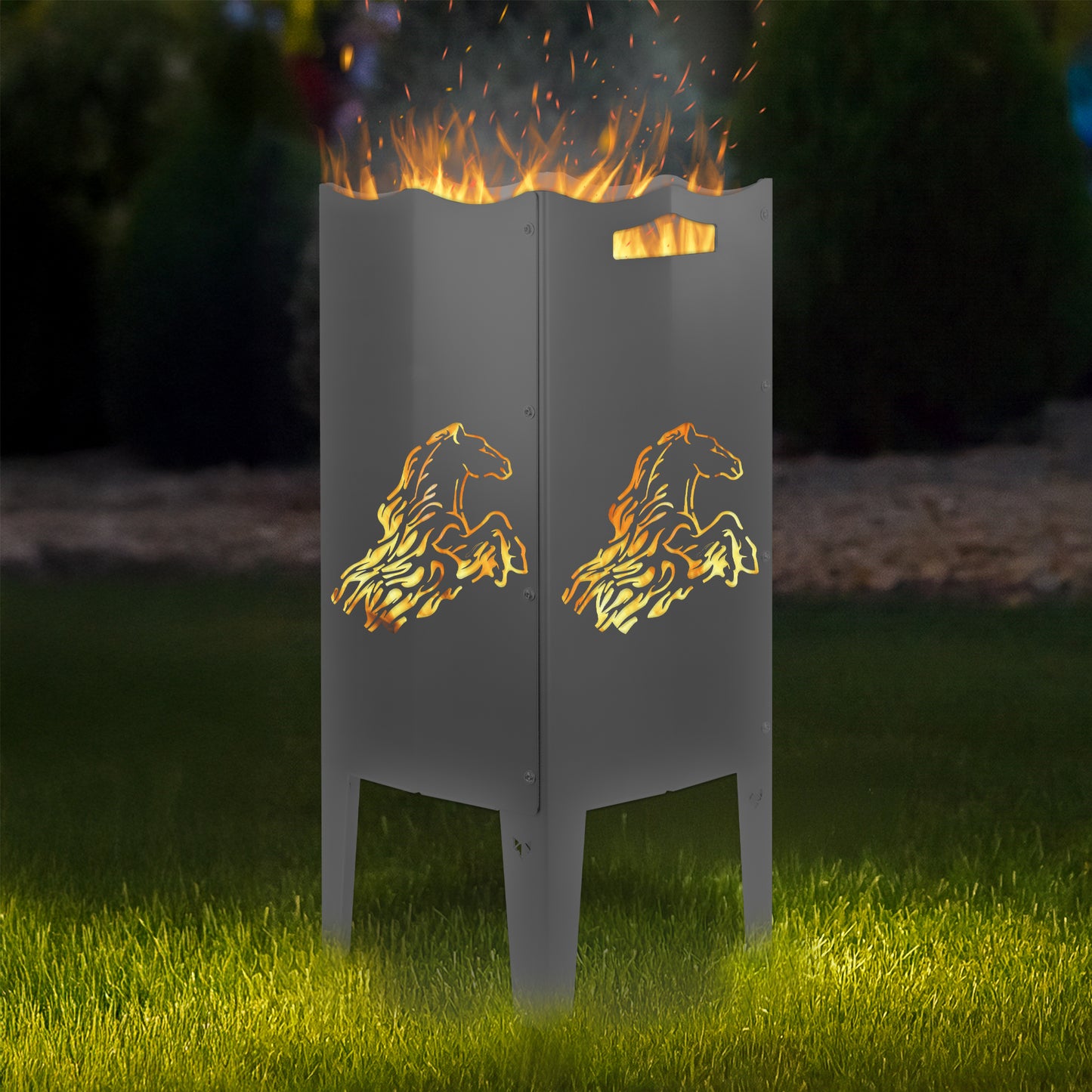 FENNEK Feuersäule Stahl mit dem Motiv Pferd - in der Feuersäule brennt ein Feuer, man sieht das Motiv sehr schön leuchten in der Abenddämmerung in einem Garten. Die Feuersäule steht auf Gras.