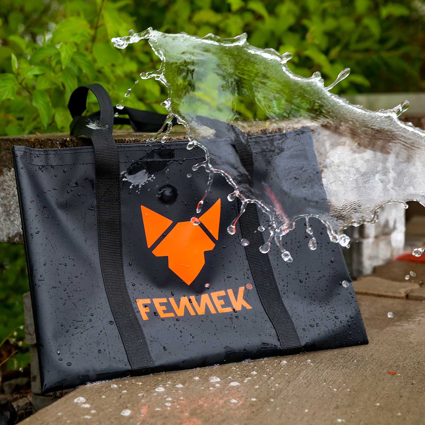 Die FENNEK Tasche steht angelehnt im Freien. Wasser wird auf die Tasche geschüttet, um den wasserabweisenden Stoff zu verdeutlichen.