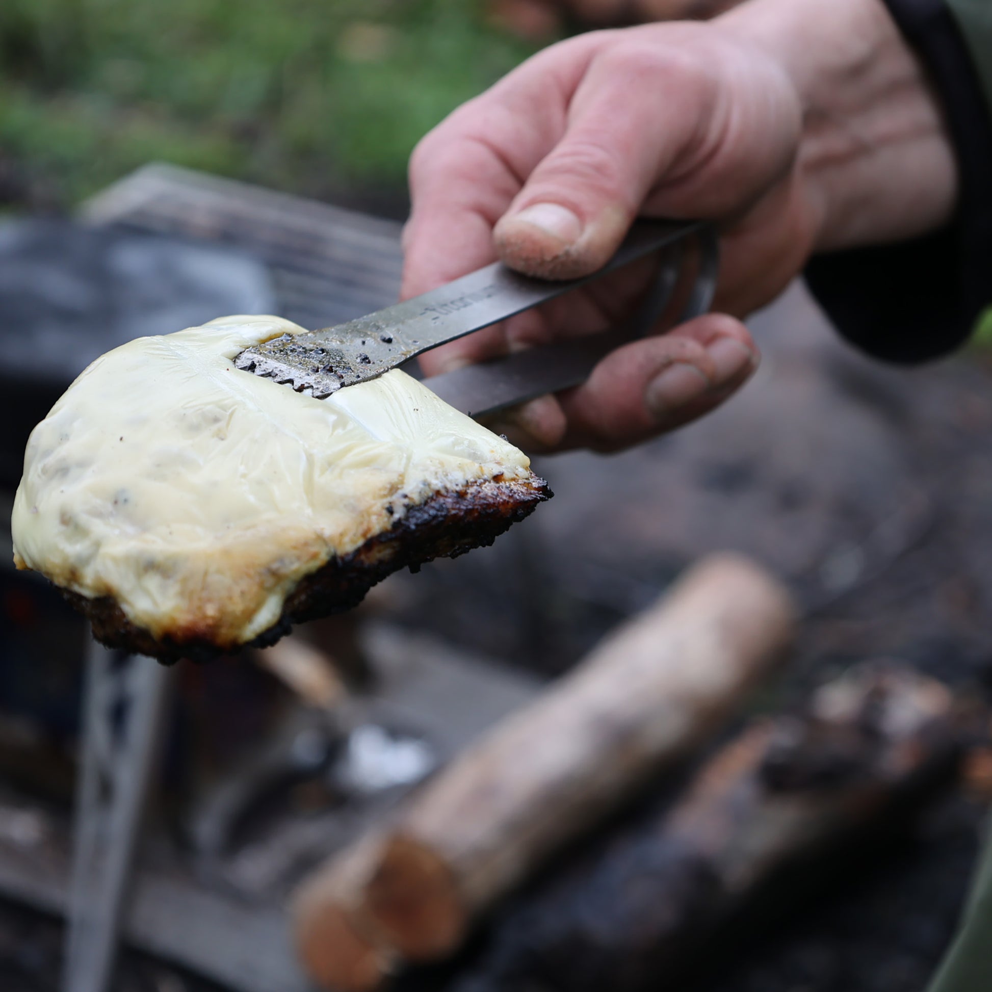 FENNEK Titan Grillzange hält einen Burgerpatty.