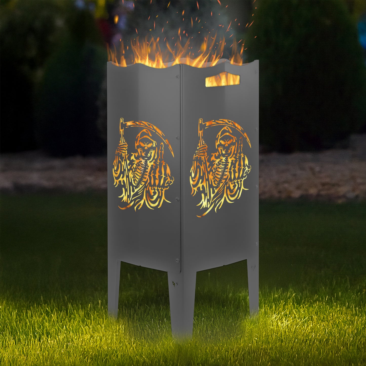 FENNEK Feuersäule Stahl mit dem Motiv Sensemann - in der Feuersäule brennt ein Feuer, man sieht das Motiv sehr schön leuchten in der Abenddämmerung in einem Garten. Die Feuersäule steht auf Gras.