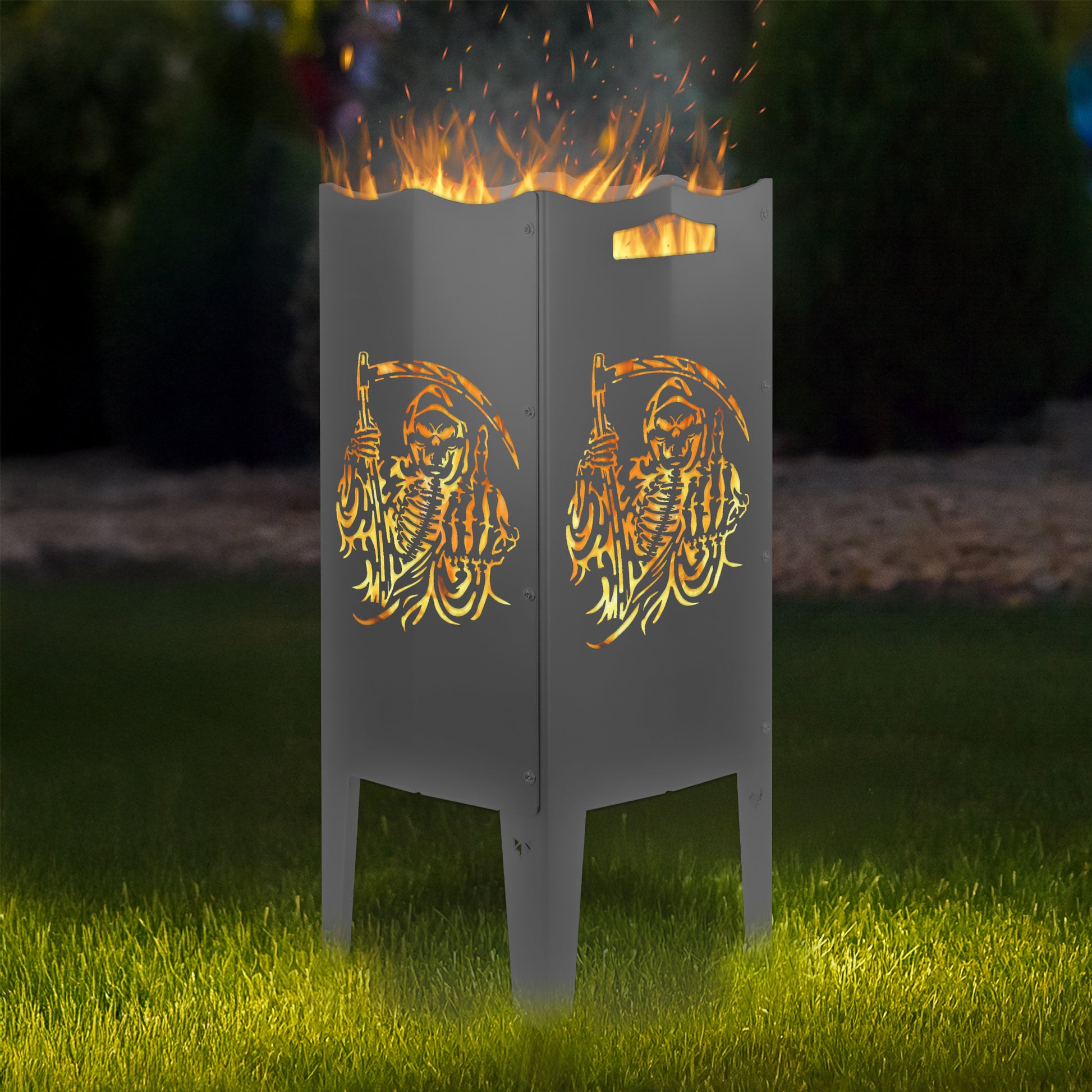 FENNEK Feuersäule Stahl mit dem Motiv Sensenmann - in der Feuersäule brennt ein Feuer, man sieht das Motiv sehr schön leuchten in der Abenddämmerung in einem Garten. Die Feuersäule steht auf Gras.