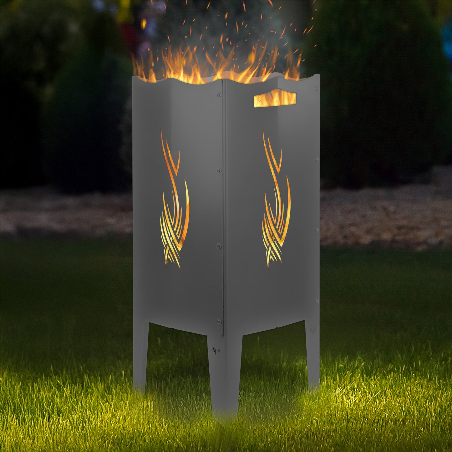 FENNEK Feuersäule Stahl mit dem Motiv Tribel - in der Feuersäule brennt ein Feuer, man sieht das Motiv sehr schön leuchten in der Abenddämmerung in einem Garten. Die Feuersäule steht auf Gras.