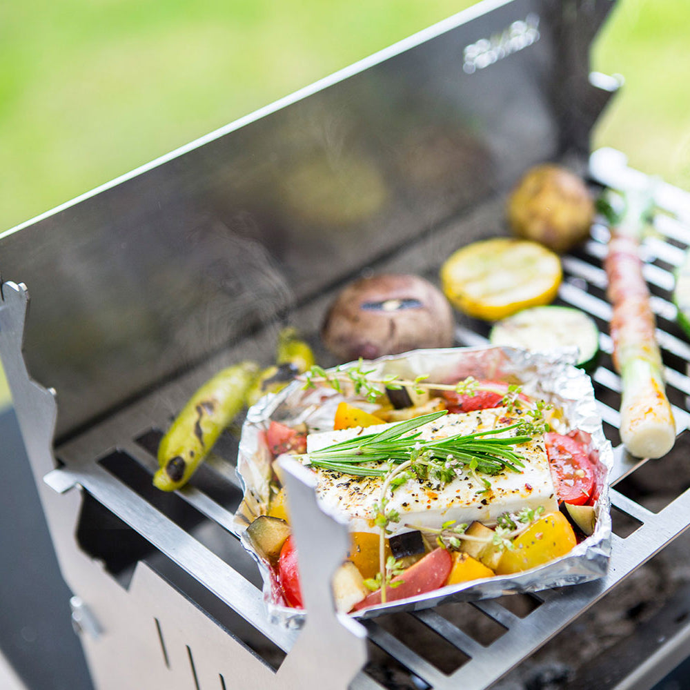 Bild zeigt den FENNEK Grill in Betrieb. Auf dem Grillrost brutzelt unter anderem Gemüse, Fleisch und Schafskäse vor sich hin.