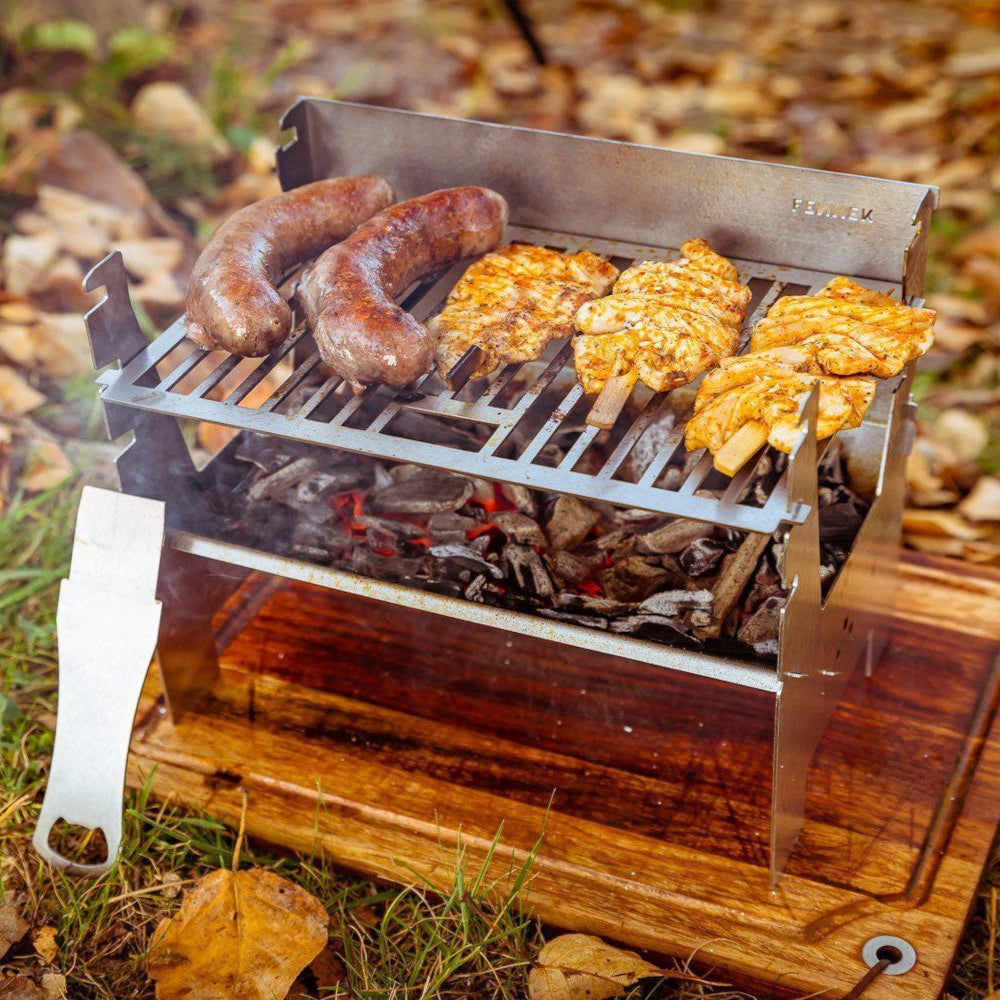 Bild zeigt den FENNEK Light im herbstlichen Ambiente in Aktion. Auf ihm grillen zwei Bratwürste und drei Hähnchenspieße.