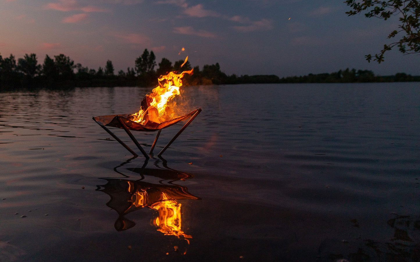 brennendes Feuer im Feuernetz das nach Sonnenuntergang im See steht und herausschaut