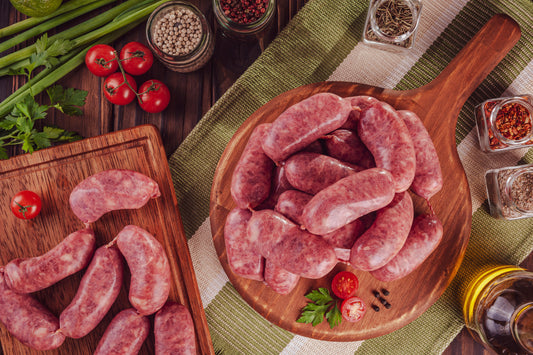 Italienische Salsiccia liegt angerichtet auf einem Holzbrett umgeben von frischem Gemüse und Gewürzen