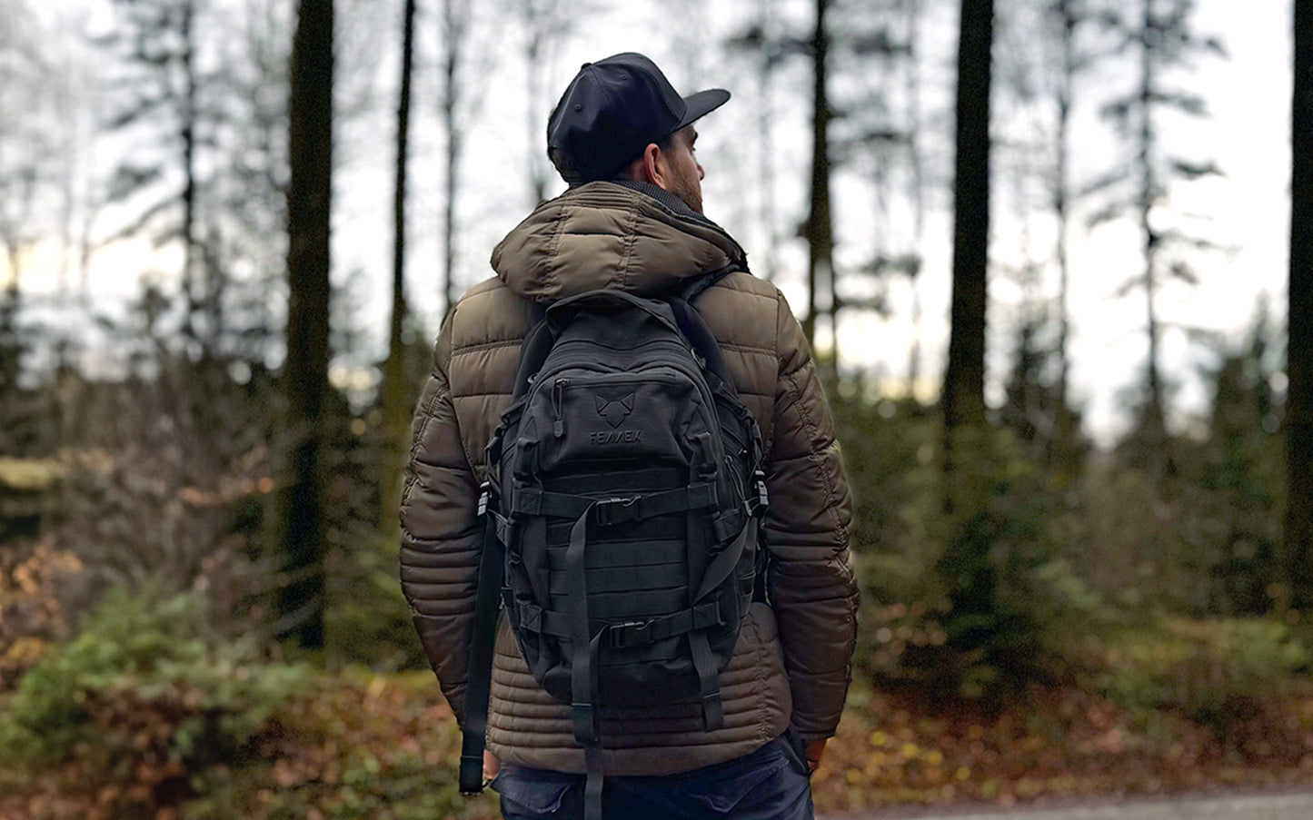 Der FENNEK Backpack One2explore wird von einem Mann getragen, der eine grüne Jacke trägt. Im Hintergrund ist Wald zu sehen.