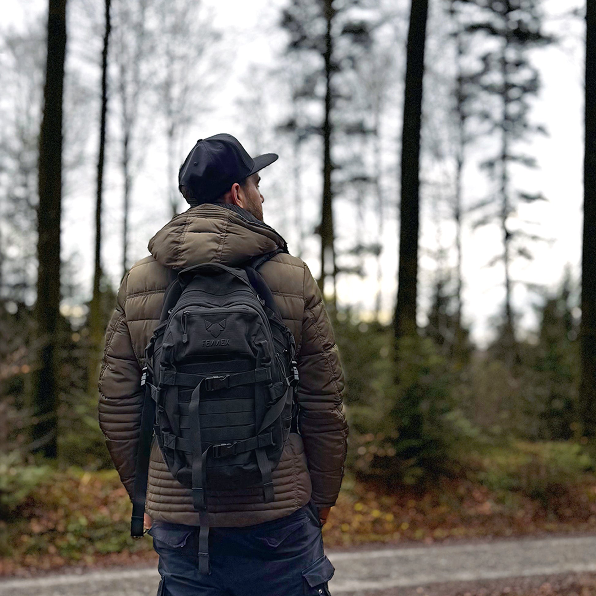 Der FENNEK Backpack One2explore wird von einem Mann getragen, der eine grüne Jacke trägt. Im Hintergrund ist Wald zu sehen.