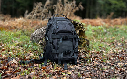 Der FENNEK Backpack On2explore am Waldrand auf dem Boden stehend. Rundherum liegt Laub. Der Rucksack lehnt an einen Baumstumpf.