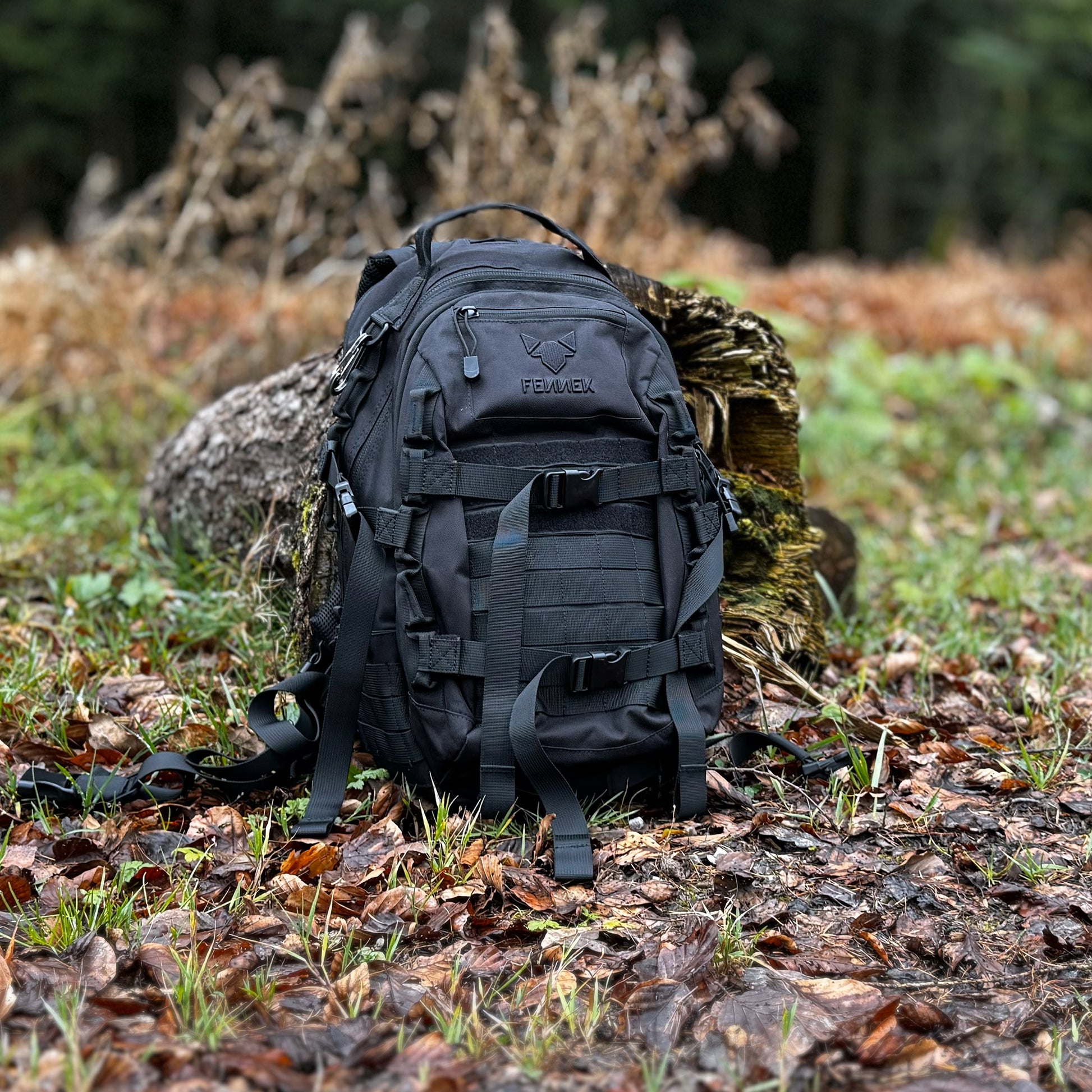 Der FENNEK Backpack On2explore am Waldrand auf dem Boden stehend. Rundherum liegt Laub. Der Rucksack lehnt an einen Baumstumpf.