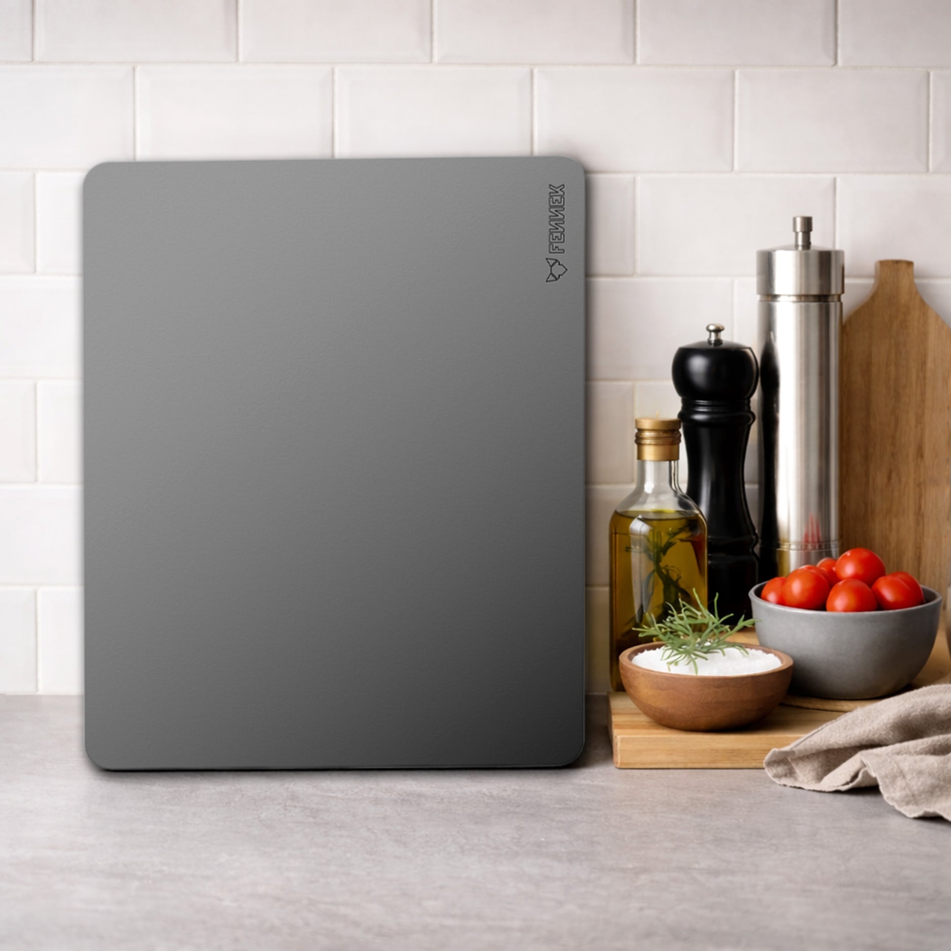 Der FENNEK Backstahl 40 x 30 cm steht senkrecht an einem Fliesenspiegel in einer Küche. Daneben steht eine Pfeffermühle, in Salzstreuer und eine Flasche mit Öl. Davor liegt ein kleines Holzschneidebrett mit Salz und Tomaten darauf. 