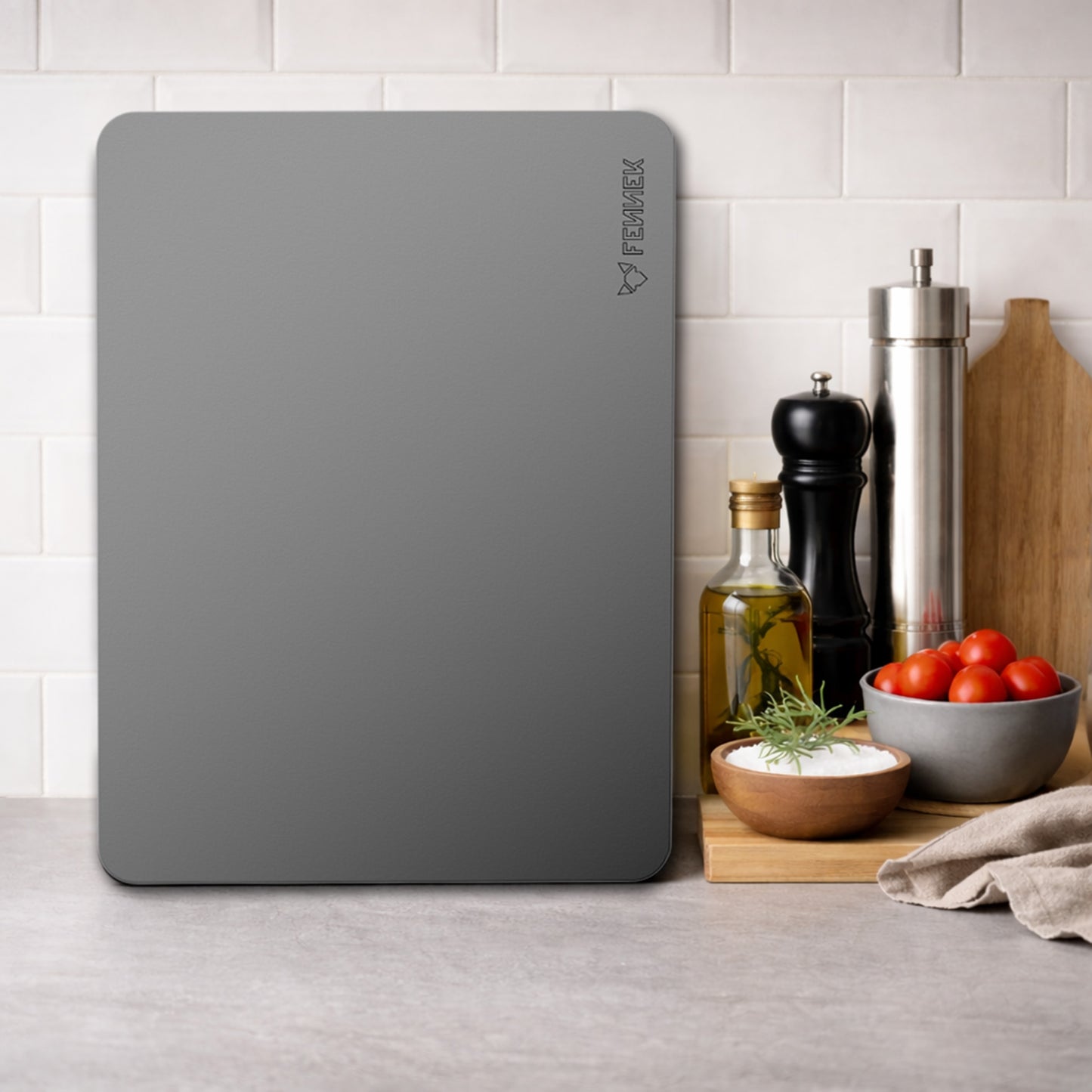 Der FENNEK Backstahl 40 x 30 cm steht senkrecht an einem Fliesenspiegel in einer Küche. Daneben steht eine Pfeffermühle, in Salzstreuer und eine Flasche mit Öl. Davor liegt ein kleines Holzschneidebrett mit Salz und Tomaten darauf. 