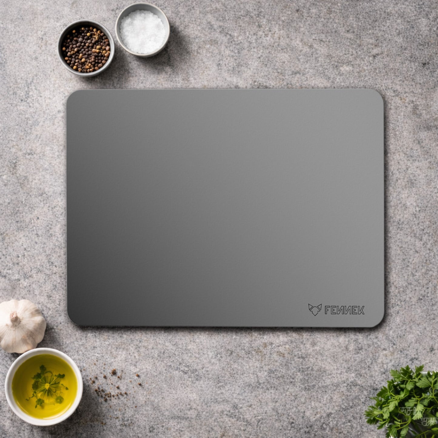 Der FENNEK Backstahl 40 x 30 cm liegt auf einer Küchenarbeitsplatte umringt von kleinen Schälchen mit Gewürzen und Kräutern.