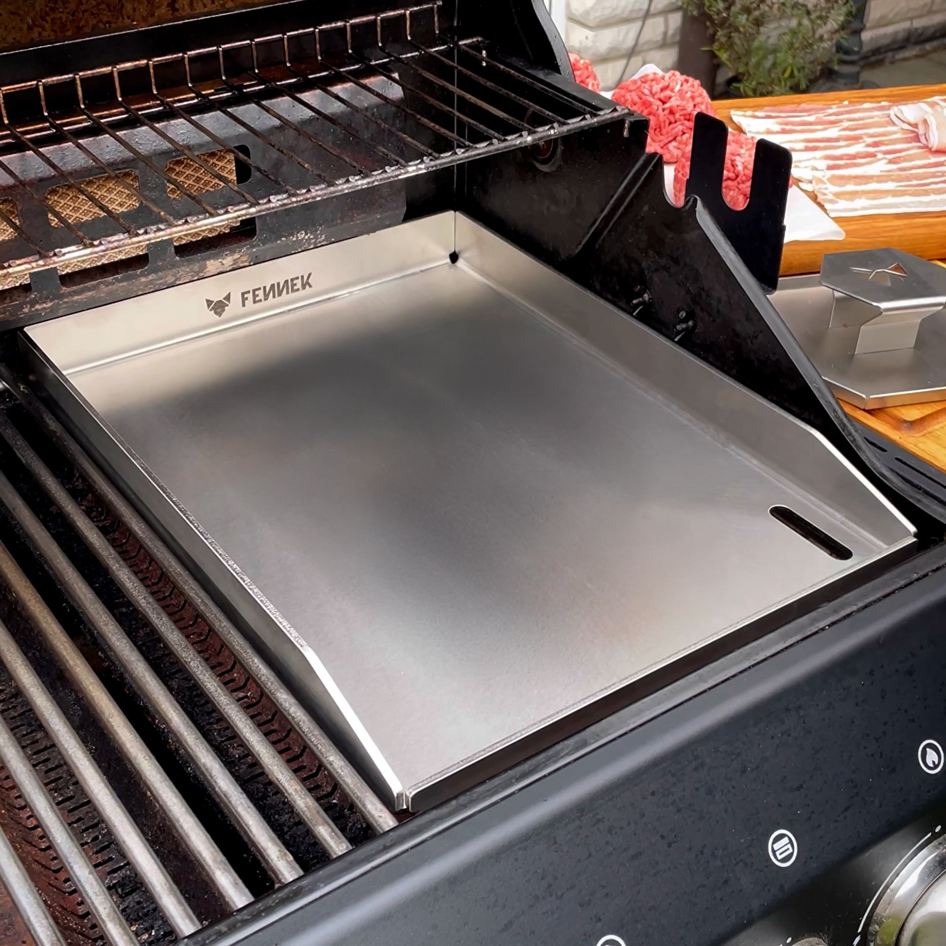 Die FENNEK Plancha 30 x 40 als Rostersatz in einem Gasgrill. Rechts auf der Ablage daneben ist der FENNEK Smasher zu sehen.