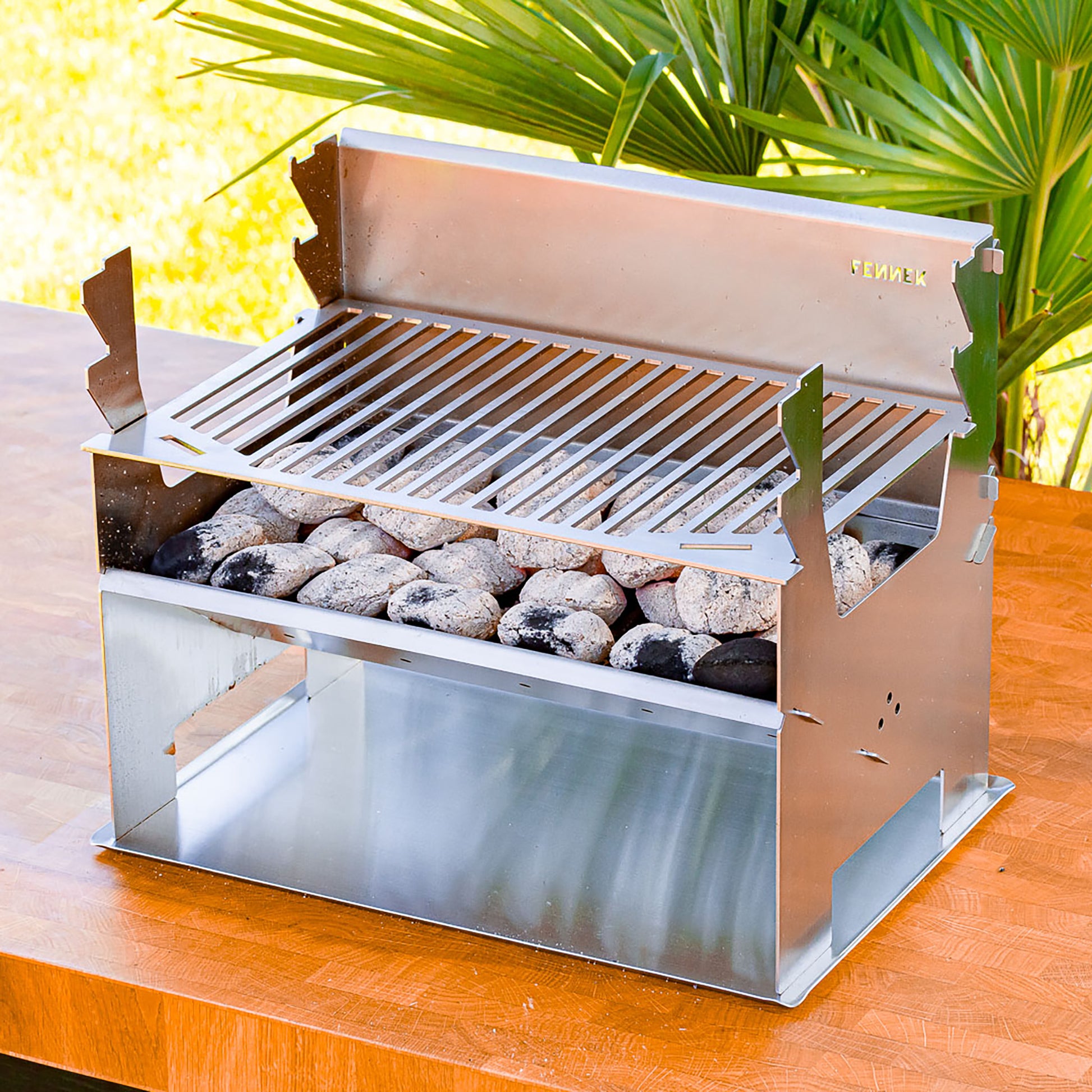 Zusammengesteckter FENNEk Holzkohlegrill steht auf dem Bodenblech das den Tisch vor Schmutz und Hitze schützt.