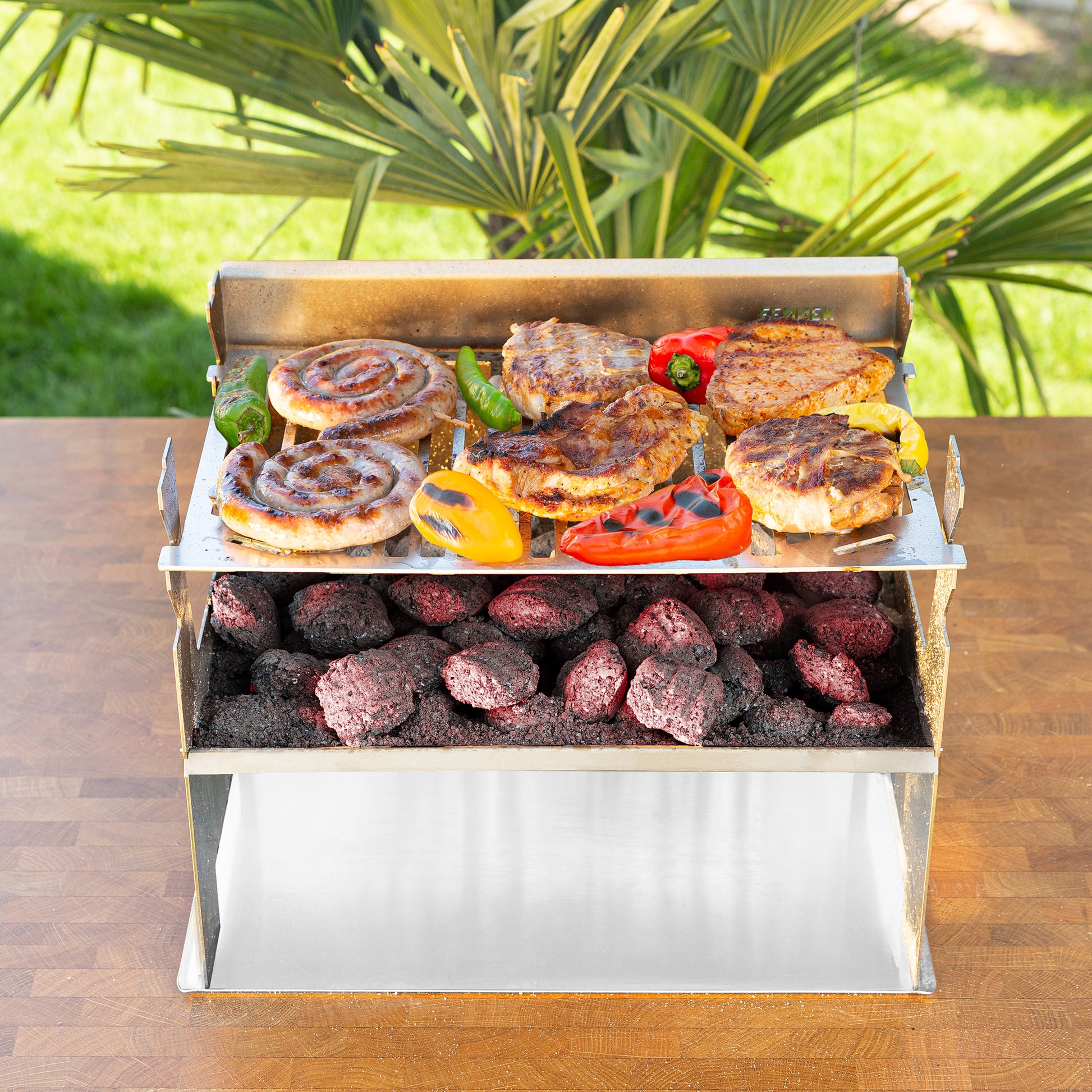 Der FENNEK 2.0 steht in einem Garten auf einem Tisch. Auf ihm brutzelt Fleisch und Gemüse.