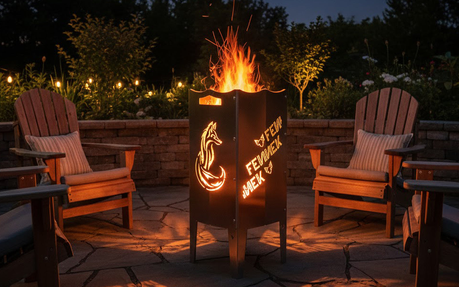 Die FENNEK Feuersäule steht brennend auf einer Terrasse. Drum herum sind Gartenstühle aufgereiht, man könnte sich schön hinsetzen und das Feuer genießen.