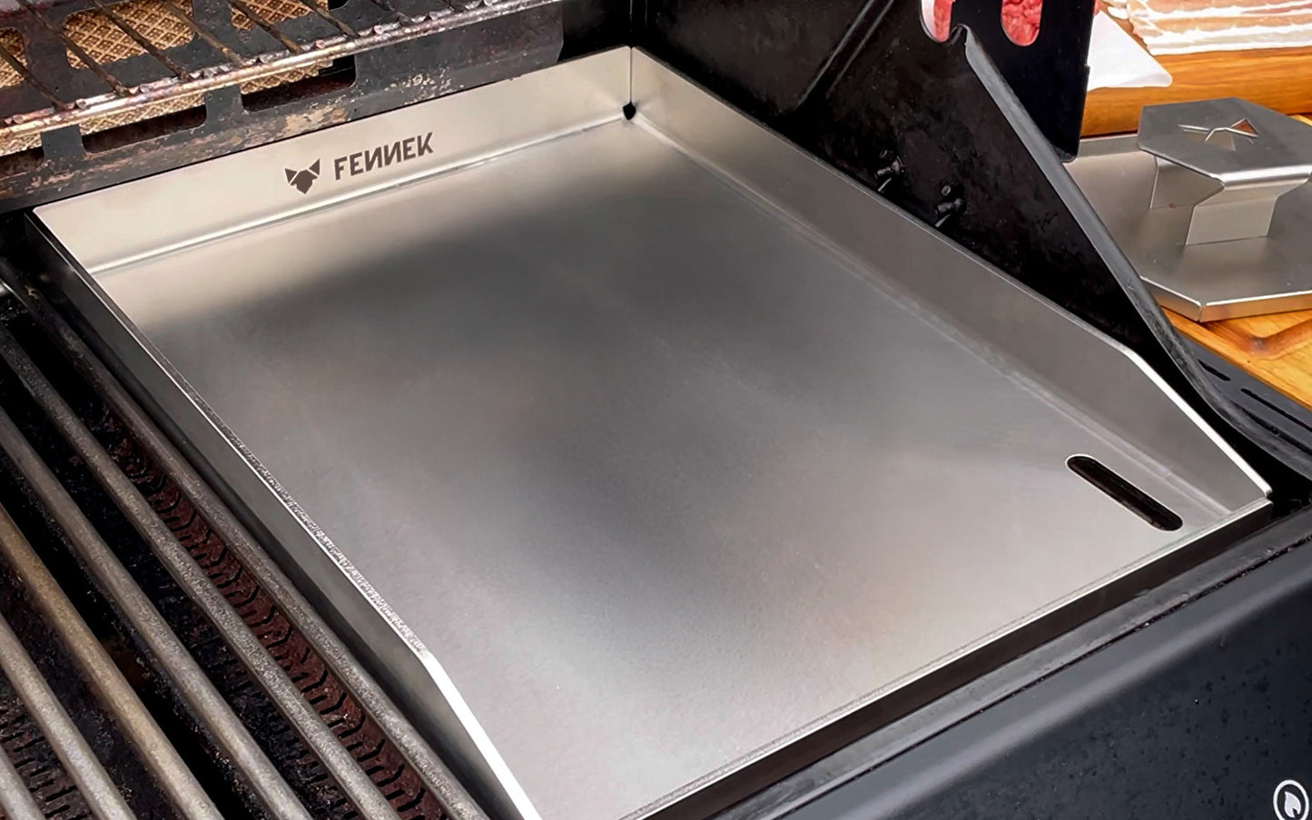 Die FENNEK Plancha 30 x 40 als Rostersatz in einem Gasgrill. Rechts auf der Ablage daneben ist der FENNEK Smasher zu sehen.