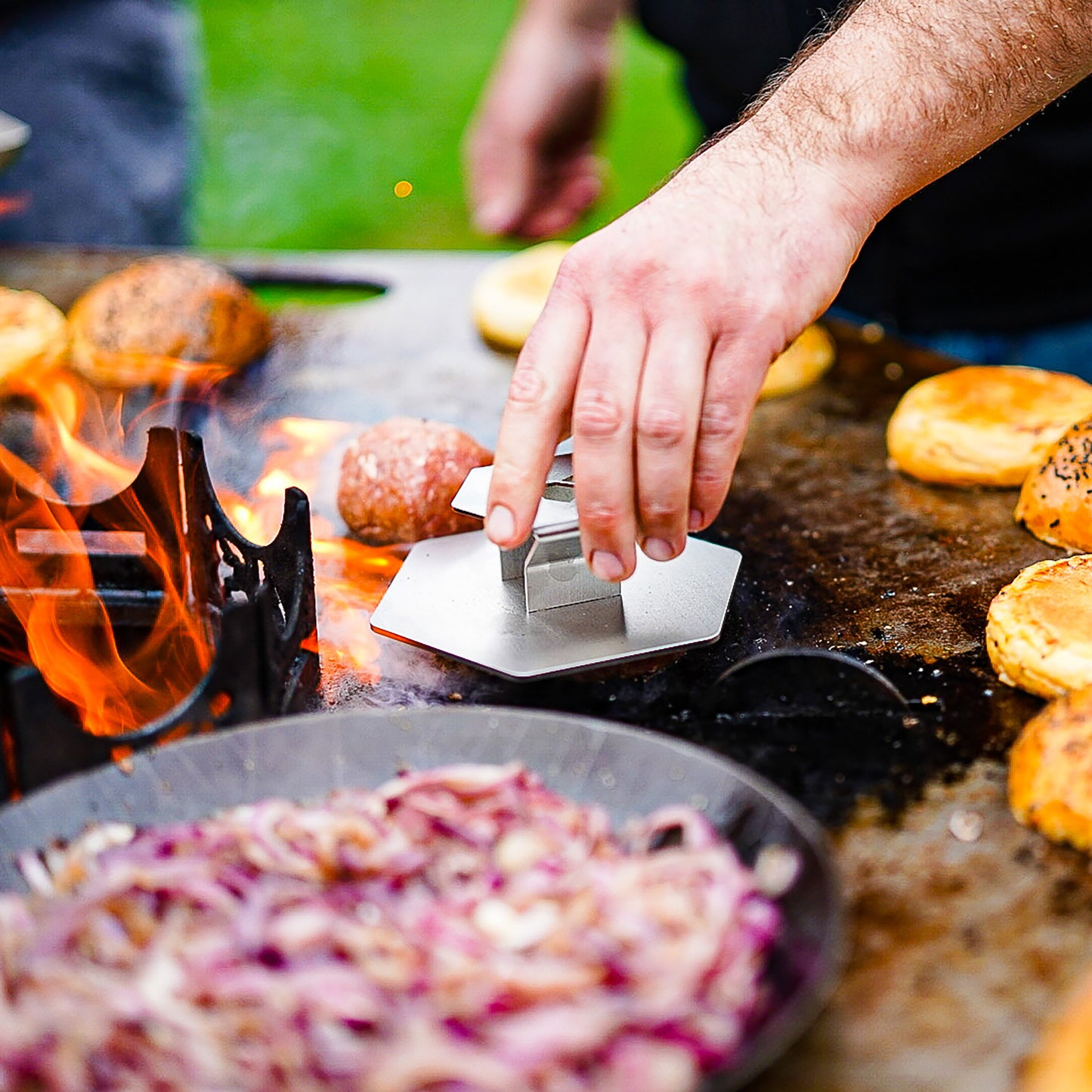 Eine Hand hält 6-eckige Hamburger Presse aus Edelstahl und presst Burger Patties auf einer großen Plancha.