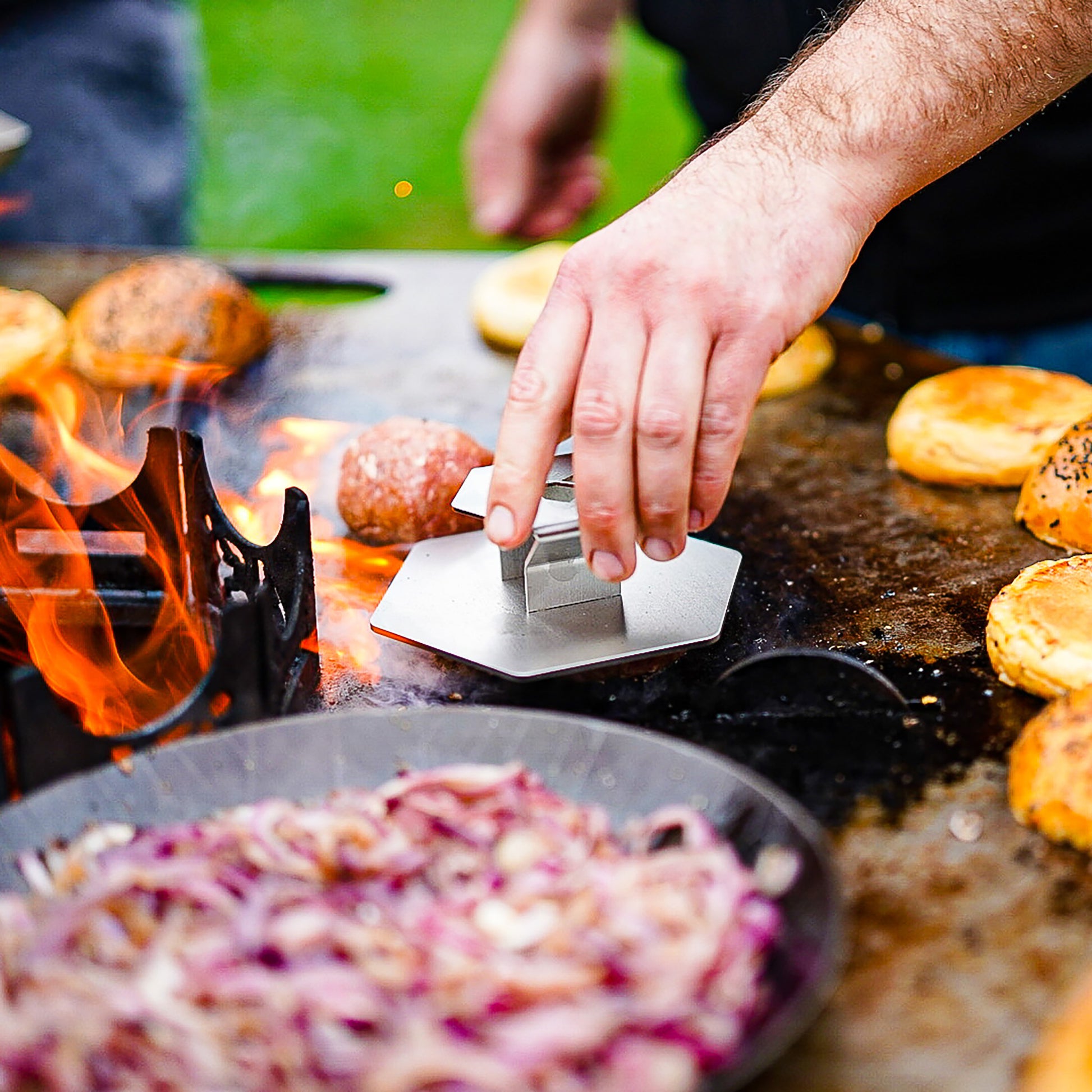 Eine Hand hält 6-eckige Hamburger Presse aus Edelstahl und presst Burger Patties auf einer großen Plancha.