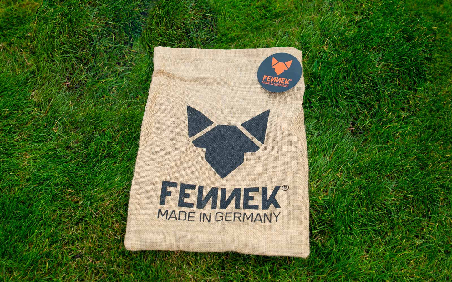 Ein Jutebeutel mit Fennek Logo-Aufdruck und einem runden Sticker darauf auf grünem Rasen.